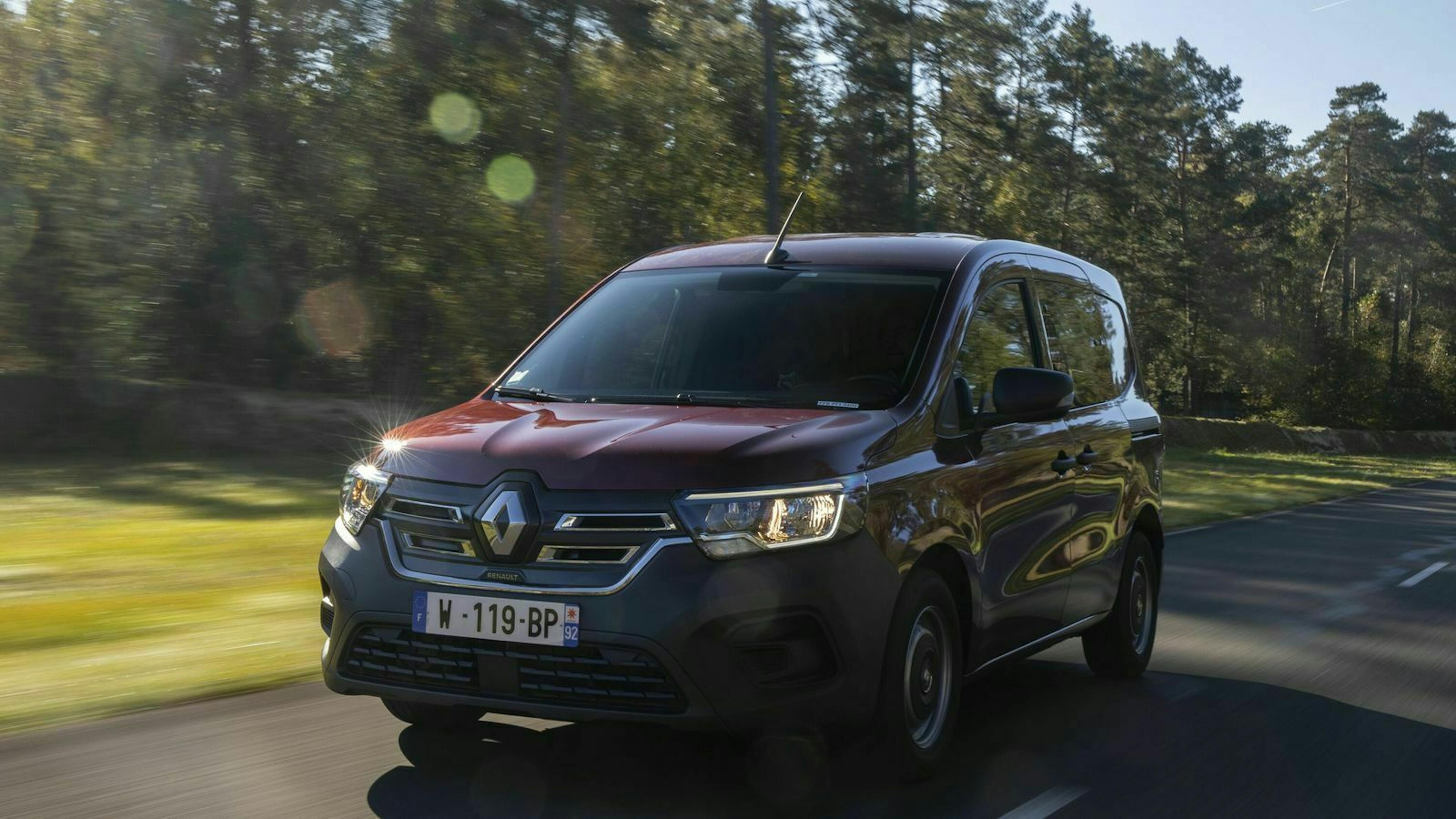 Ein weinroter Renault Kangoo Z.E. fährt eine Landstraße entlang an einem Wald vorbei