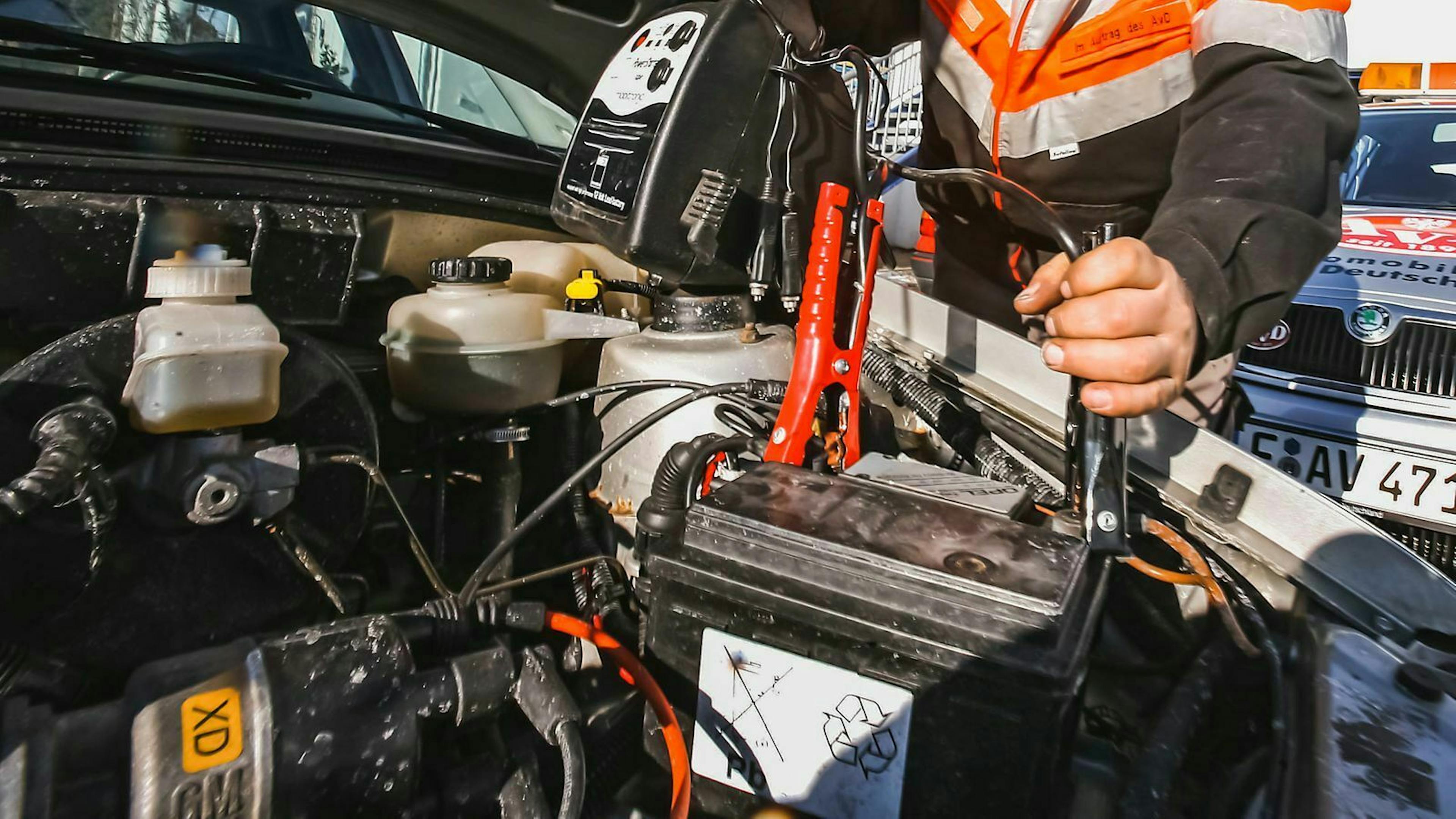 Ein Mitarbeiter eines Fachbetriebs klemmt ein Überbrückungsgerät an eine Autobatterie an.