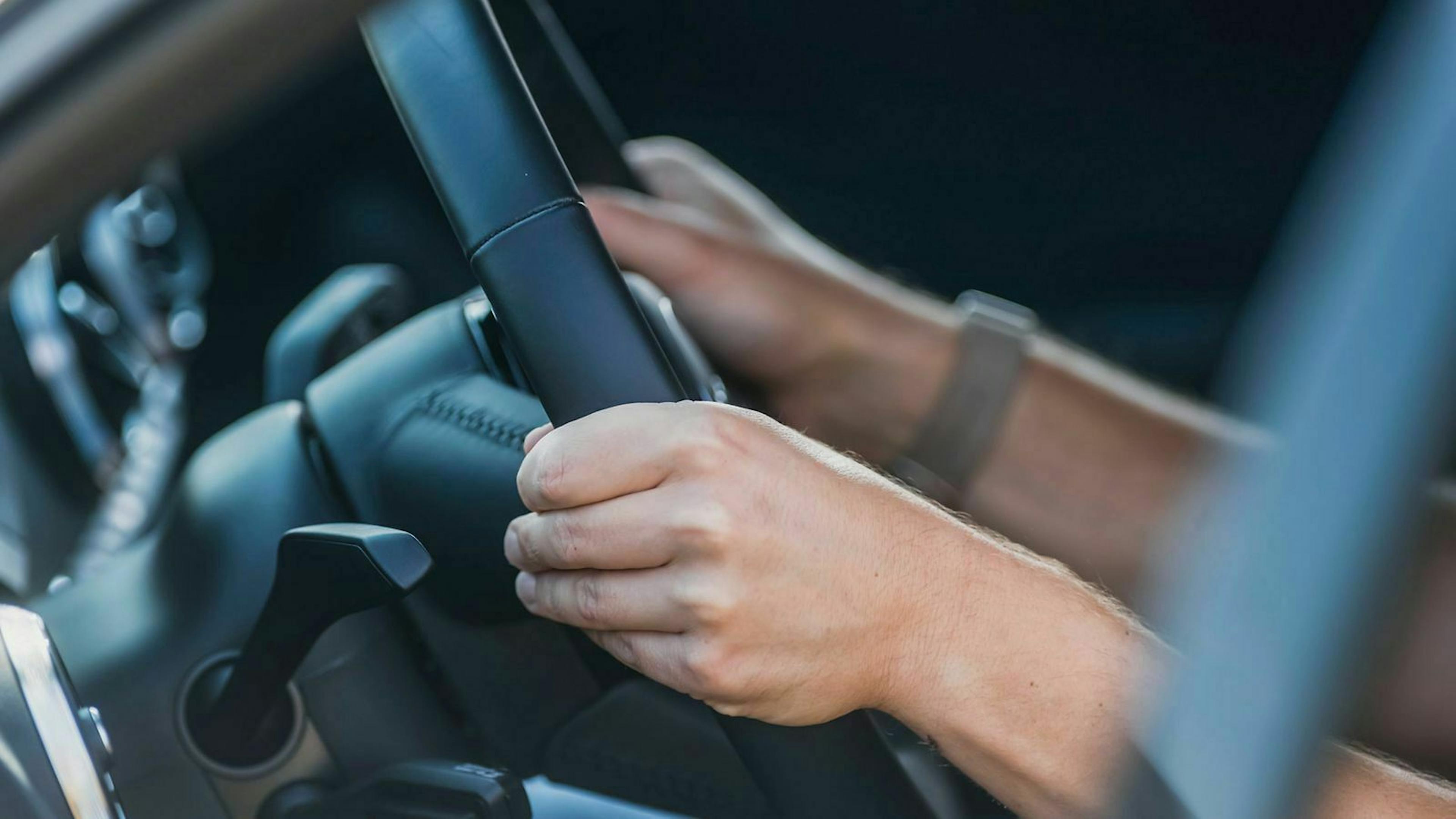 Hände am Lenkrad eines Autos. 