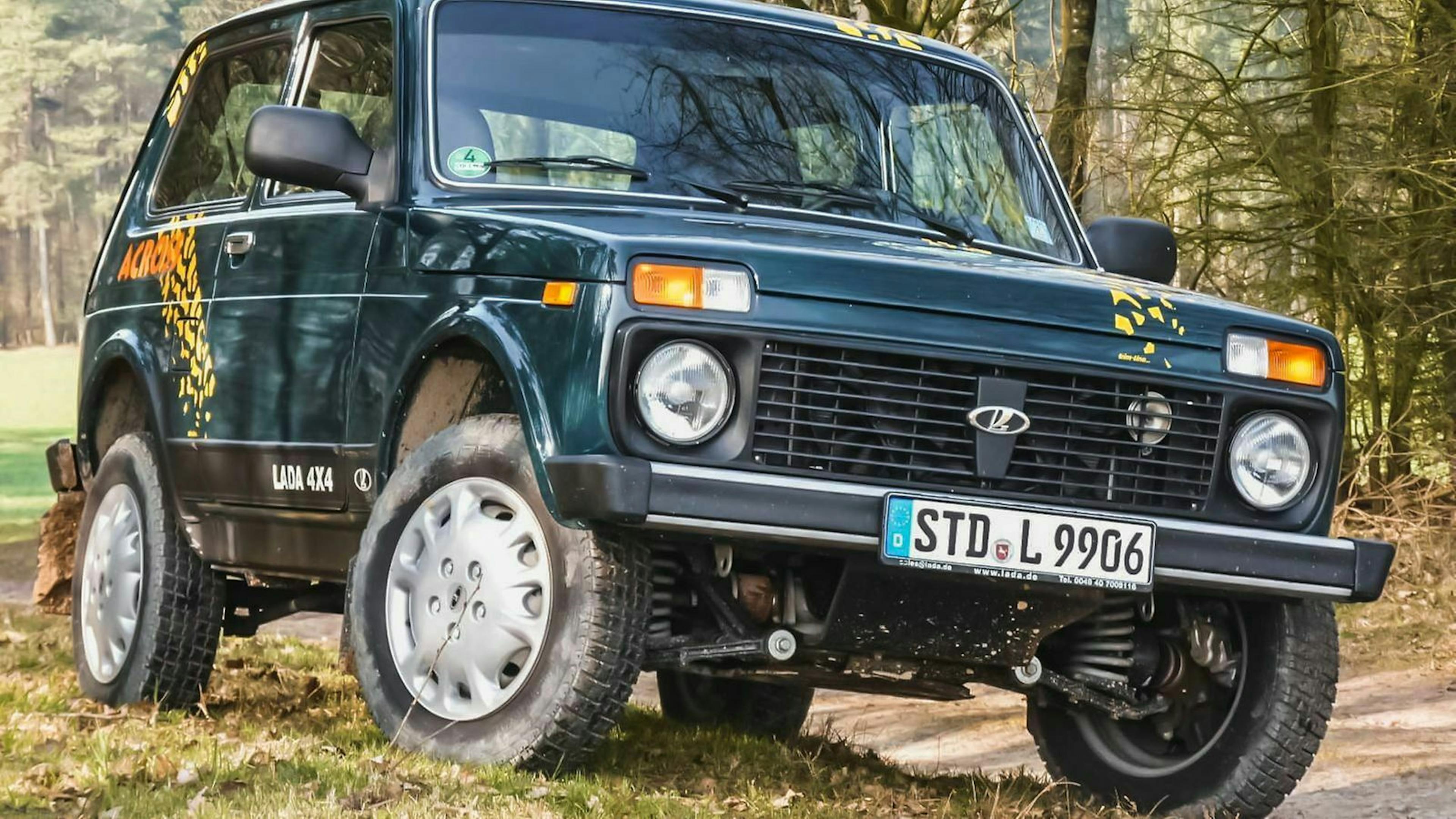 Ein Lada Niva steht auf einer Wiese mit eingeschlagenen Rädern.