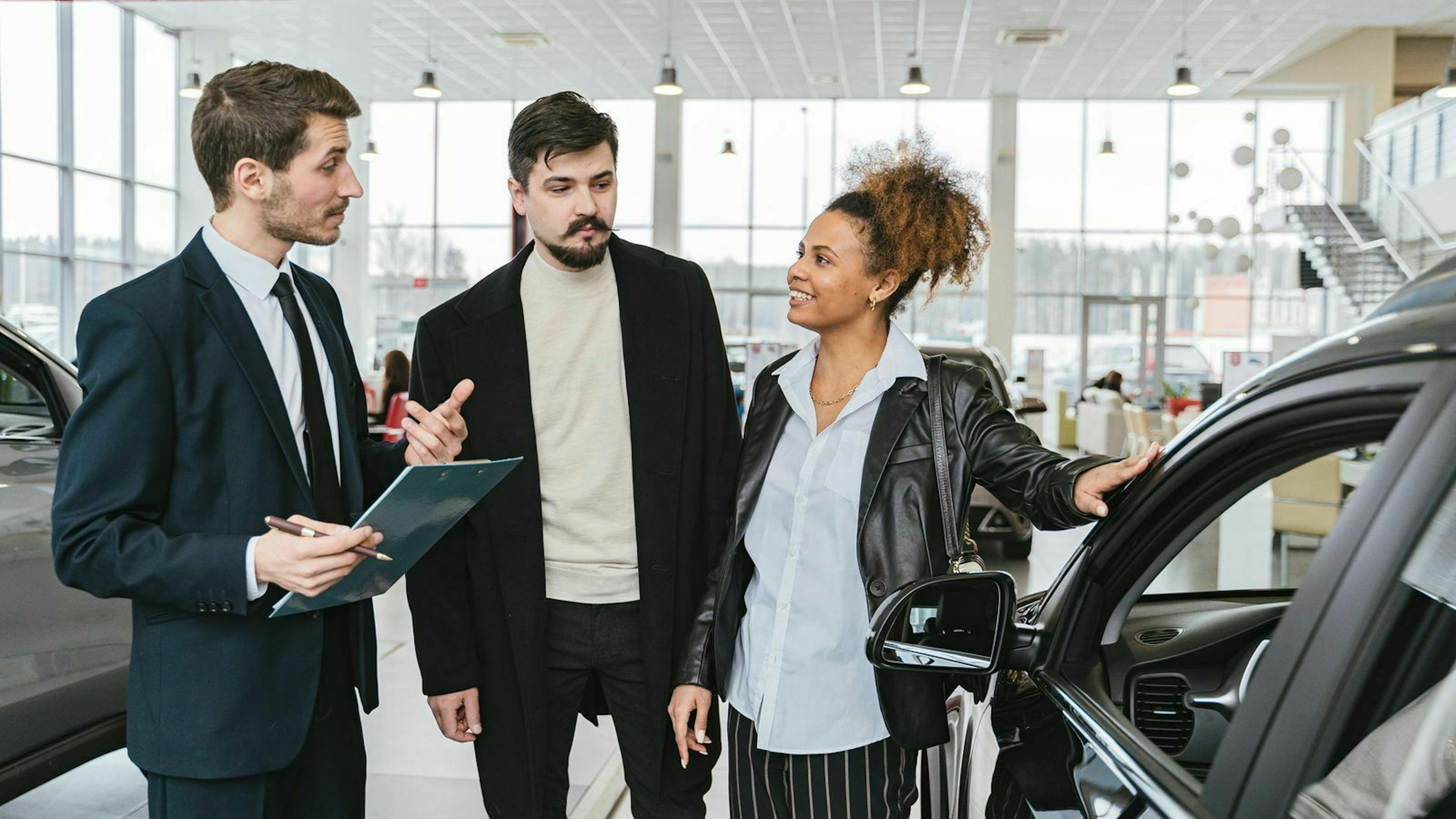 Drei Personen stehen im Showroom eines Autohauses und betrachten einen PKW