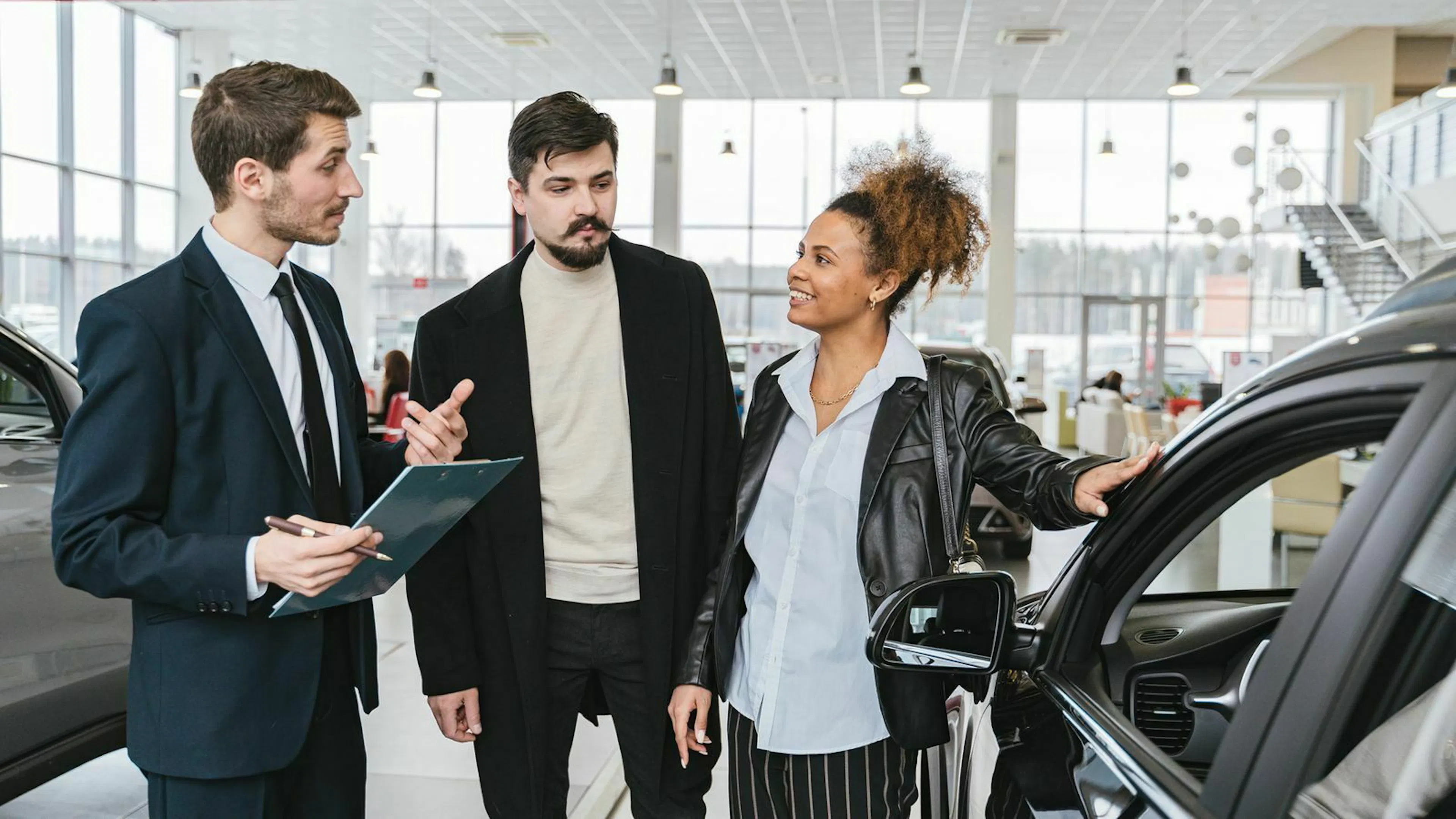 Drei Personen stehen im Showroom eines Autohauses und betrachten einen PKW