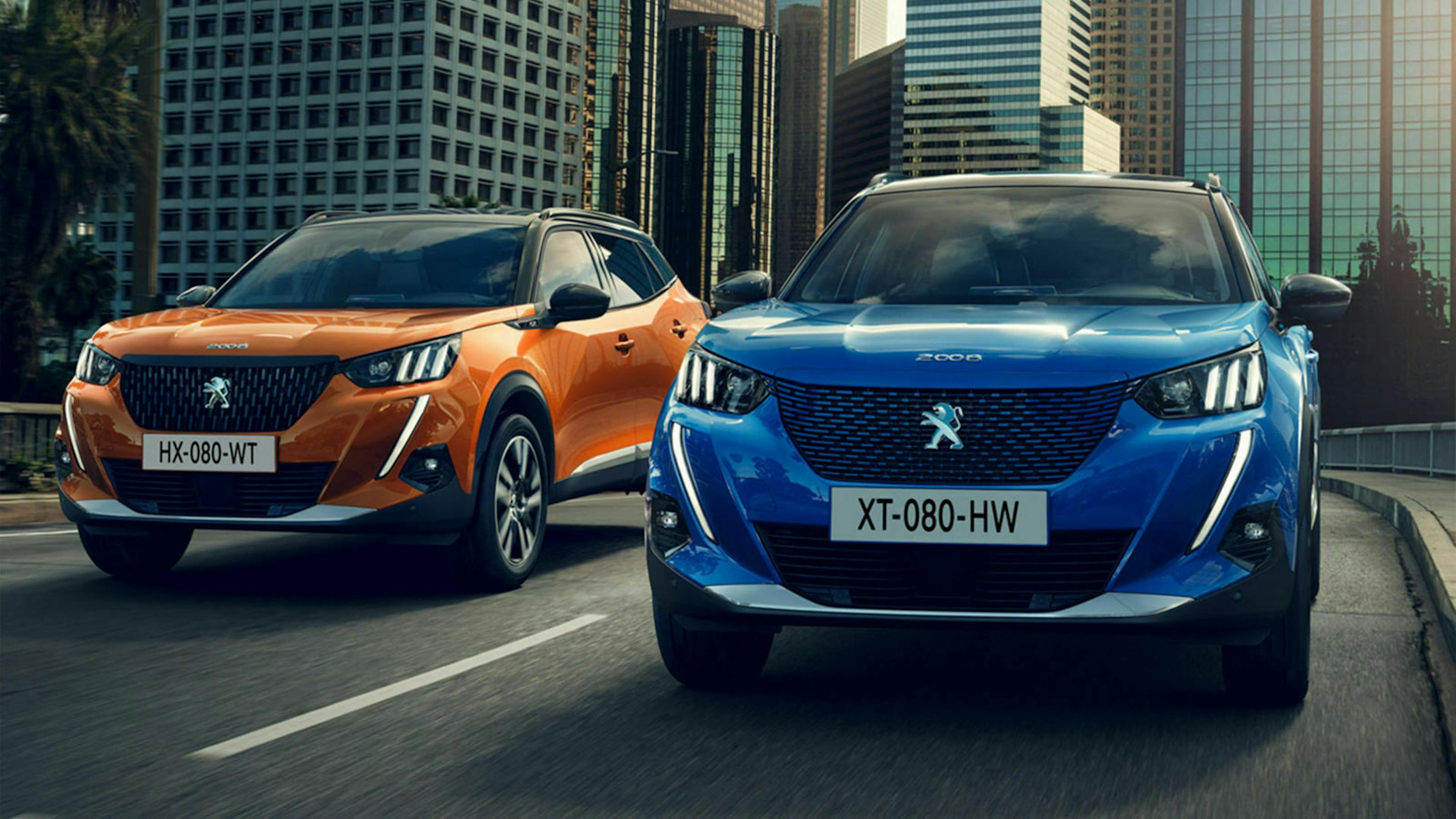 Ein blauer und ein orangener Peugeot 2008 fahren über eine Straße in einer Innenstadt vor Bürogebäuden