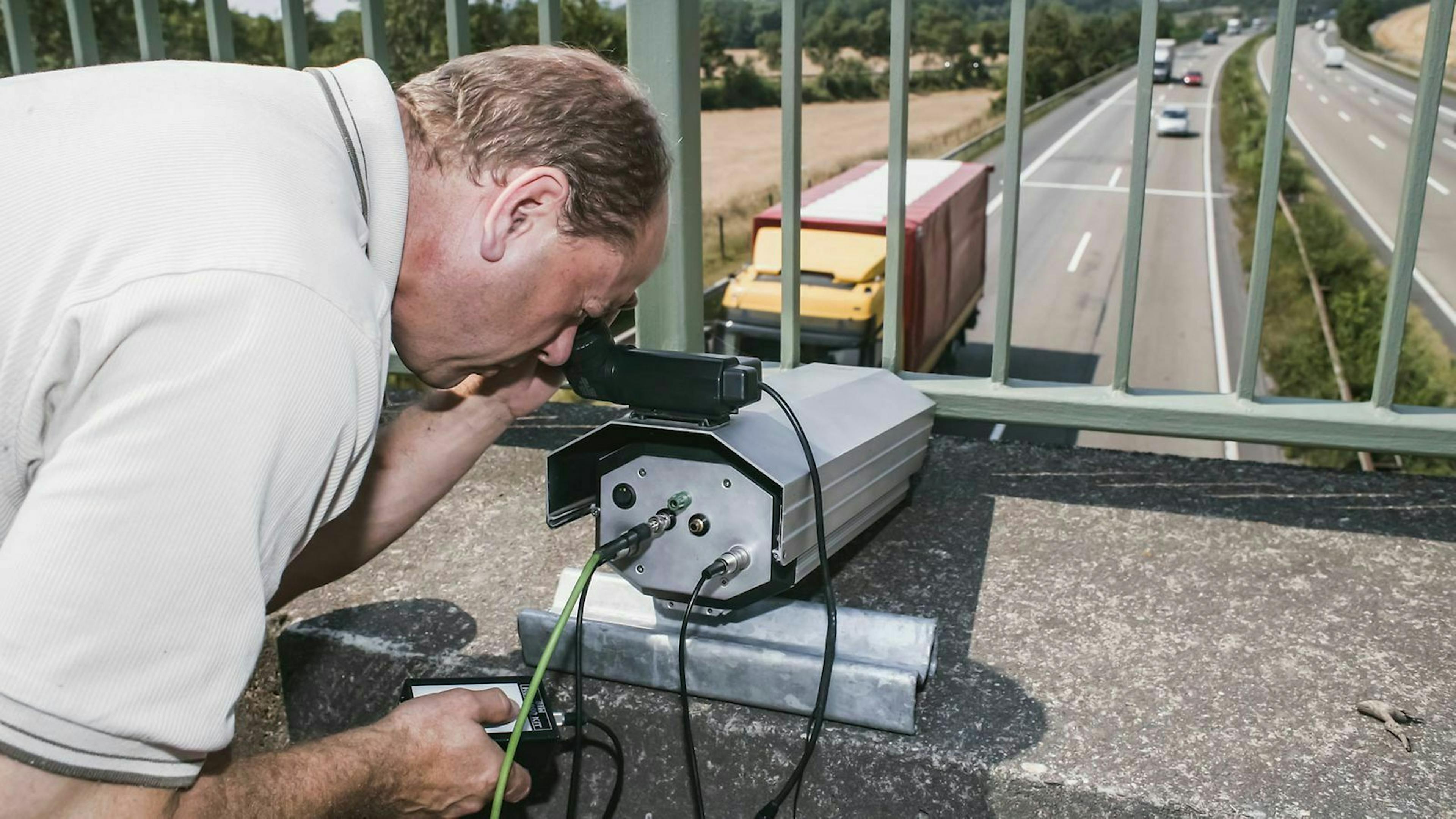 Ein Mann misst mit einem speziellen Gerät den Abstand von Fahrzeugen von einer Autobahnbrücke aus.