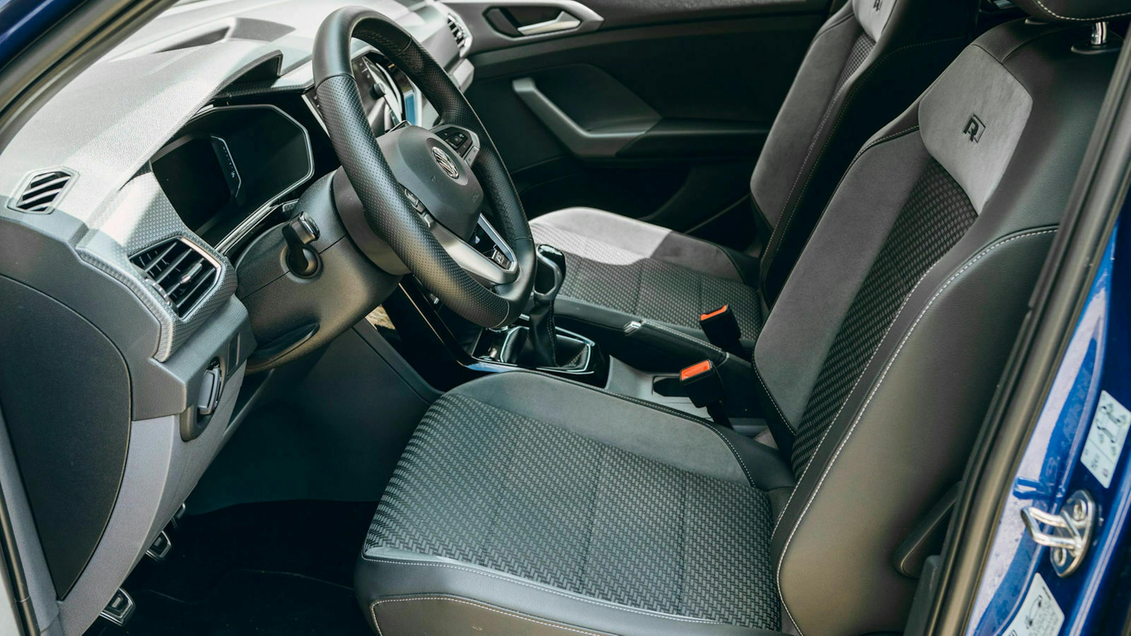 Innenraum eines Autos mit modernen, grauen Stoff- und Kunstledersitzen, einem Lenkrad und einer Konsole mit Touch-Bedienelementen.