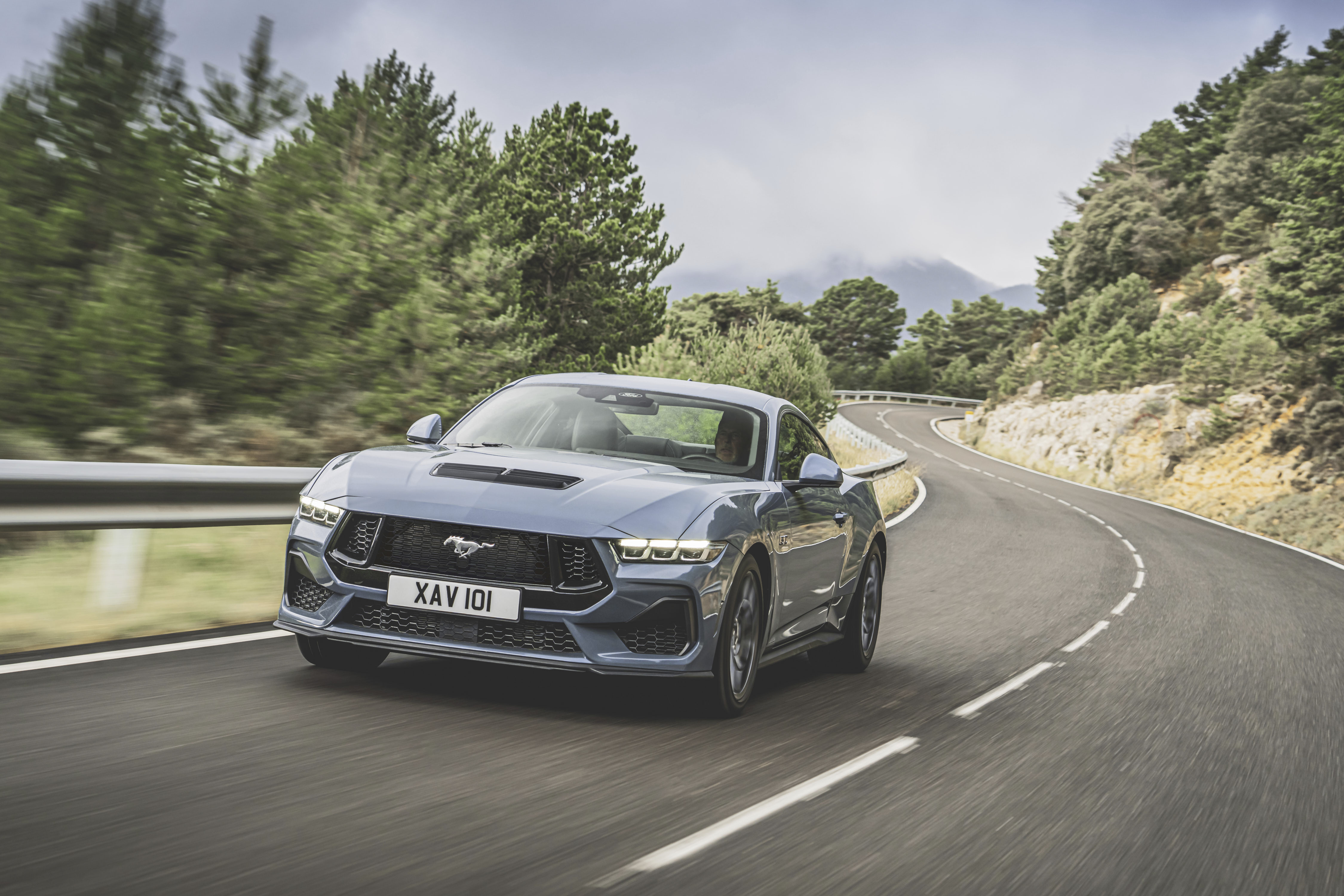 Ein Ford Mustang GT fährt dynamisch auf einer Bergstraße, Frontansicht.