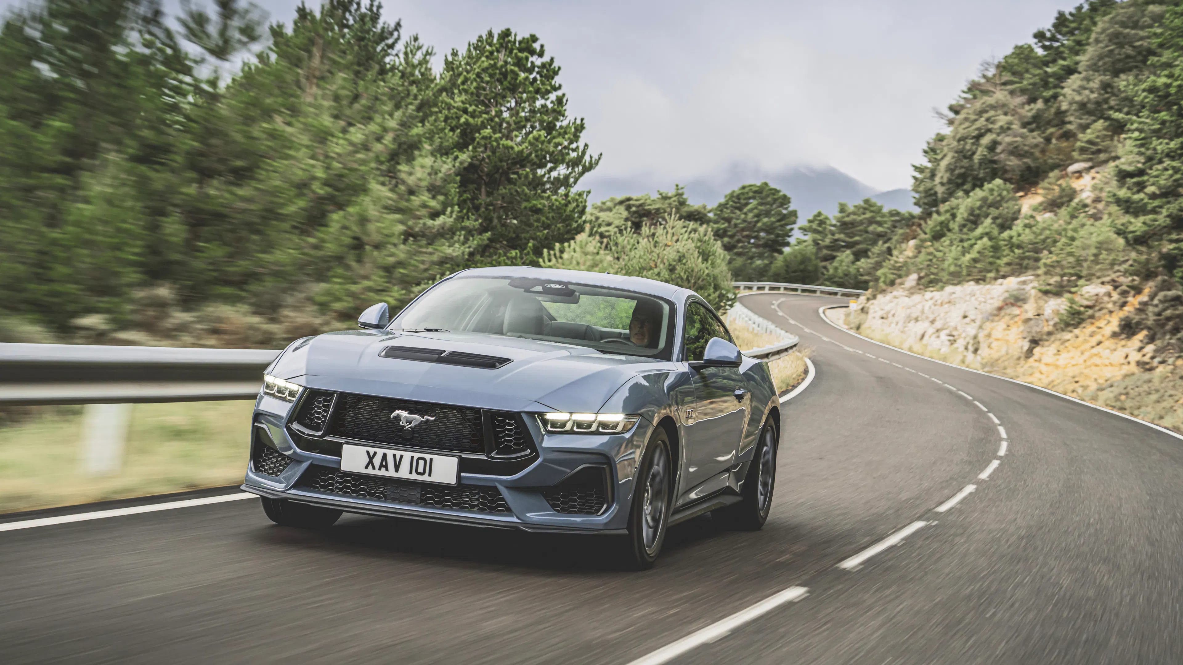 Ein Ford Mustang GT fährt dynamisch auf einer Bergstraße, Frontansicht.