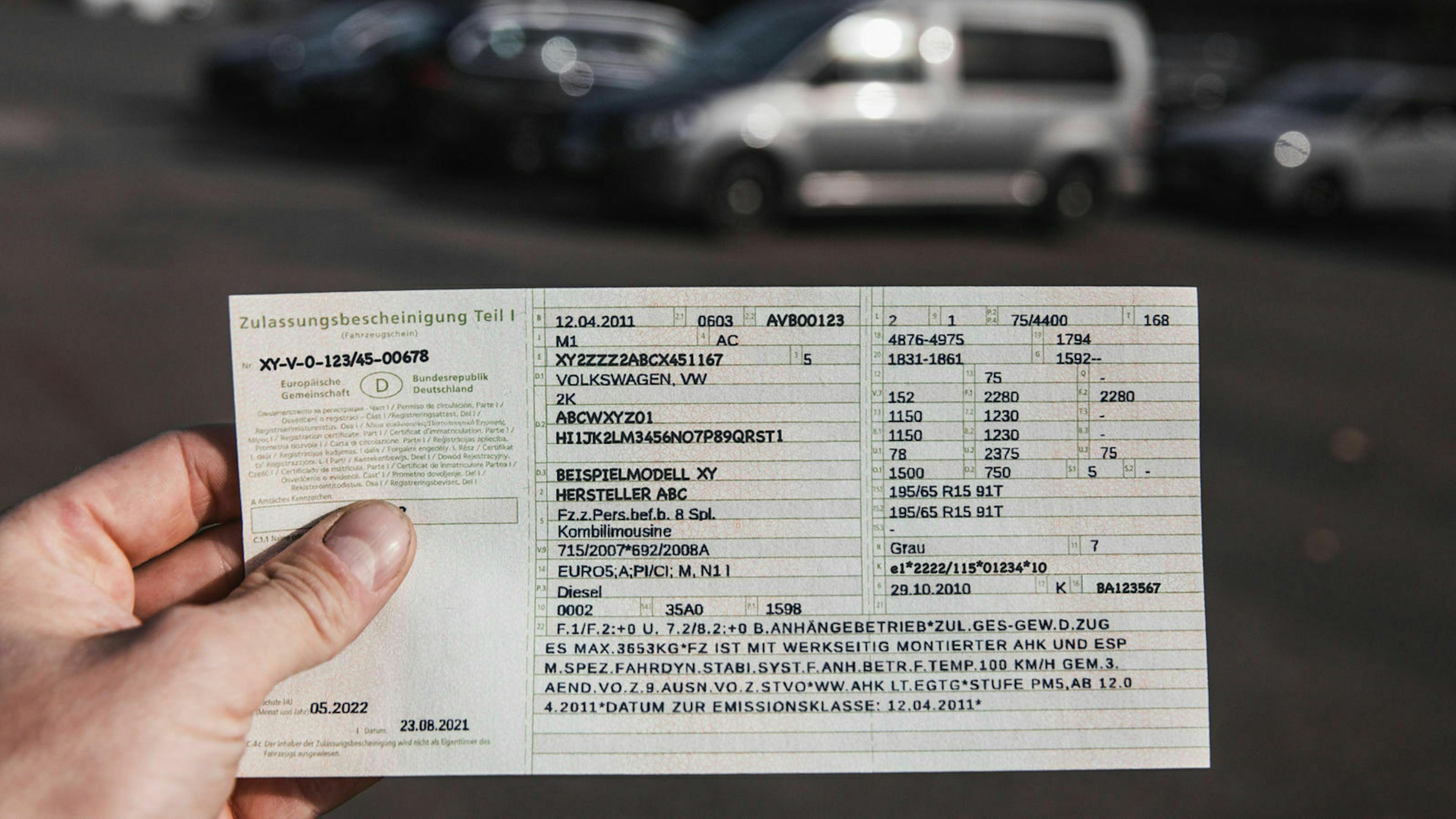 Jemand hält die Zulassungsbescheinigung Teil 1, früher Fahrzeugschein, in der Hand