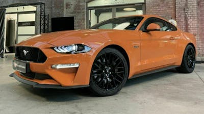 Ein orangefarbener Ford Mustang steht in einer Lagerhalle