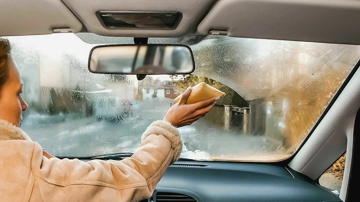Eine Frau wischt die Windschutzscheibe ihres Autos von innen ab.