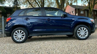 Ein dunkelblauer Mitsubishi ASX steht auf einem steinigen Untergrund vor einer Häuserfront mit Bäumen
