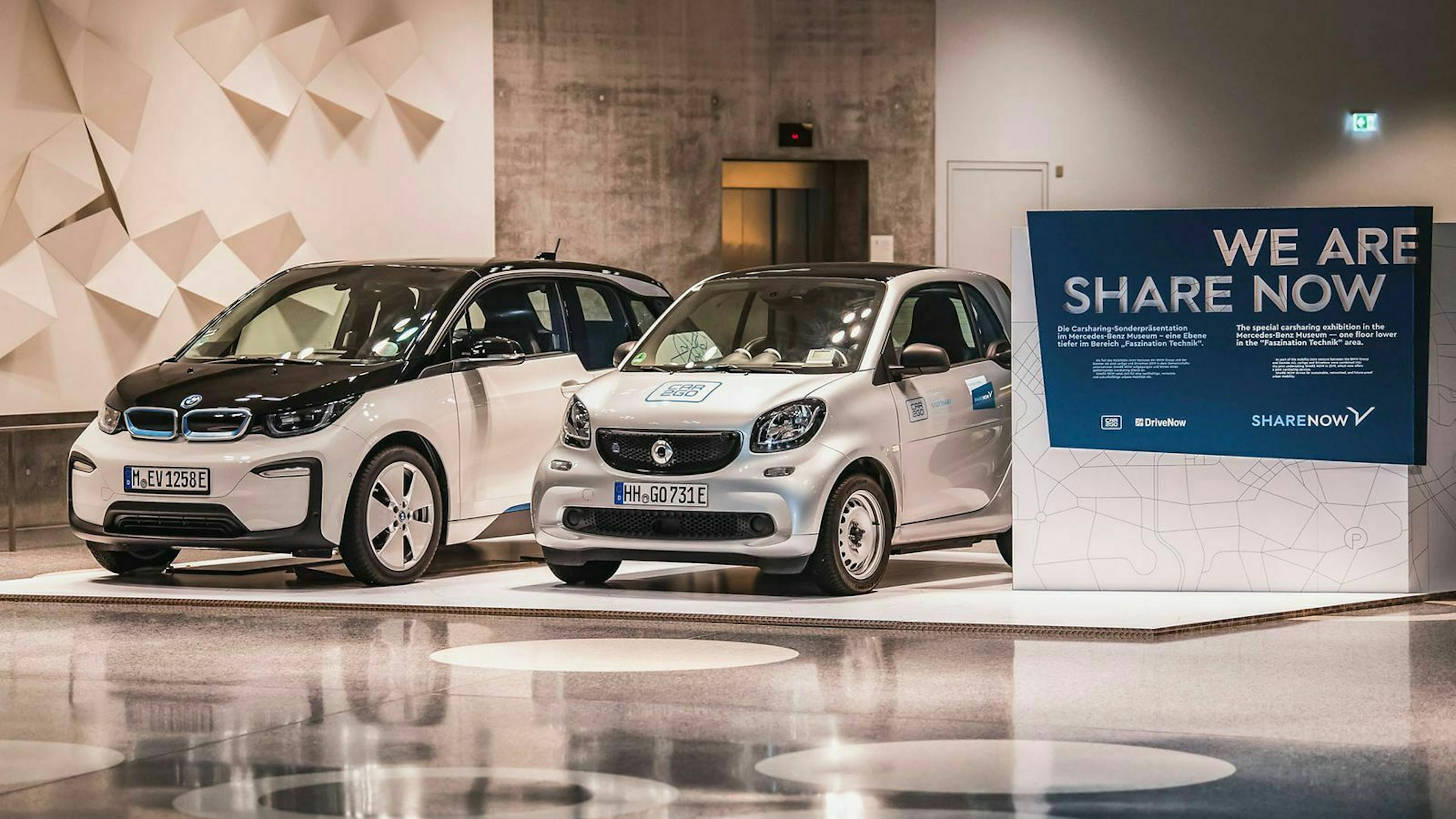 Ein Smart und ein BMW i3 stehen in einer Messehalle am Stand von ShareNow nebeneinander.