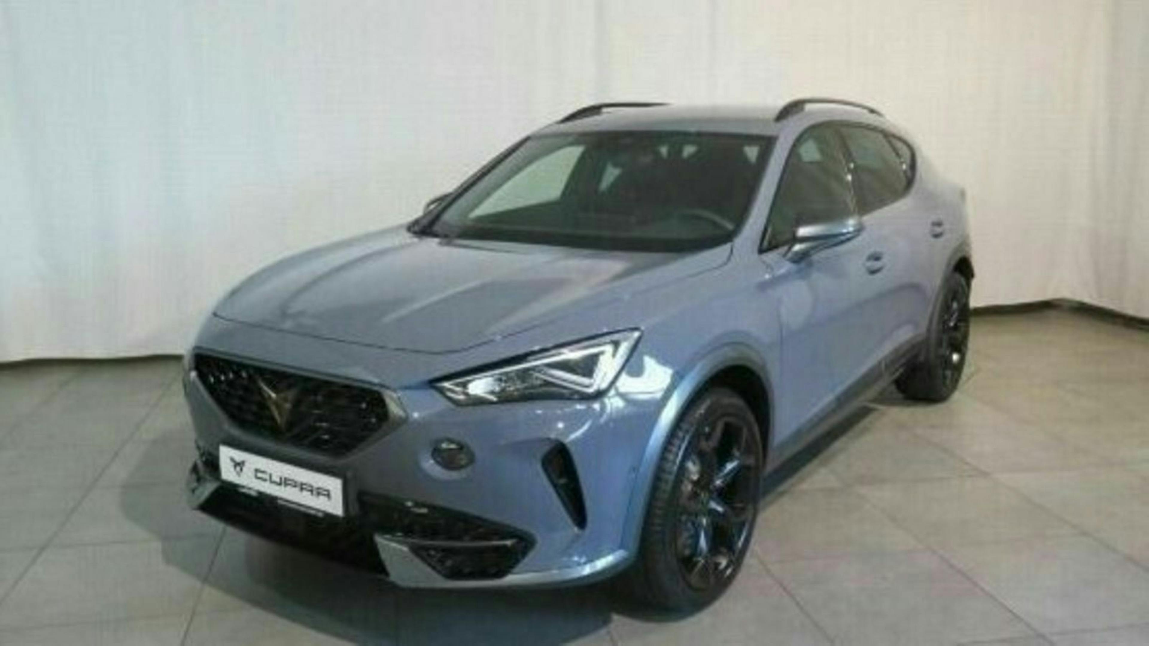 Blauer Cupra-SUV mit sportlichem Design, schwarzen Felgen und Frontspoiler, auf grauem Boden vor weißem Hintergrund.