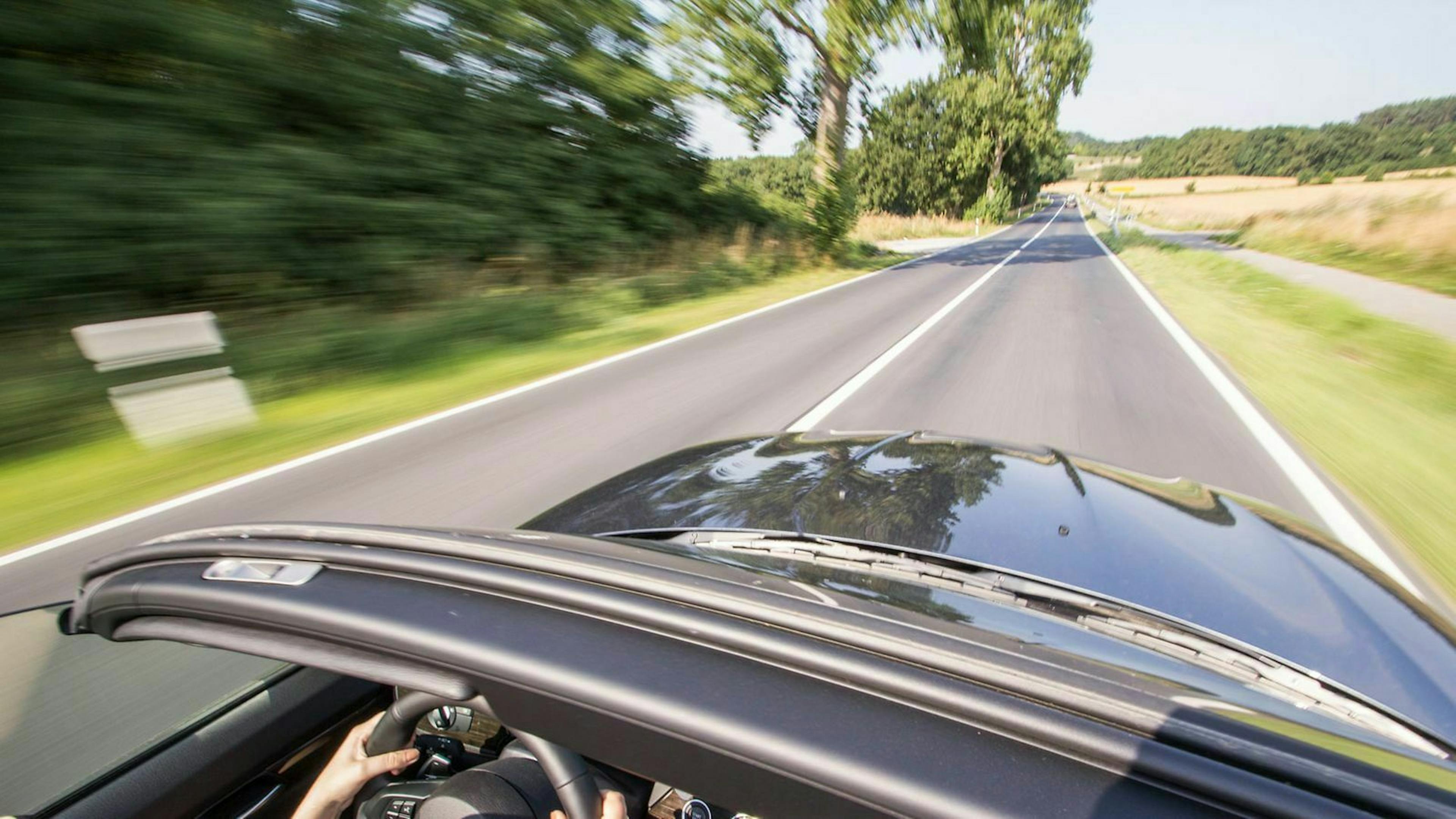 Ein Cabrio fährt auf einer sommerlichen Landstraße und verbraucht dabei weniger Sprit als innerorts oder auf der Autobahn