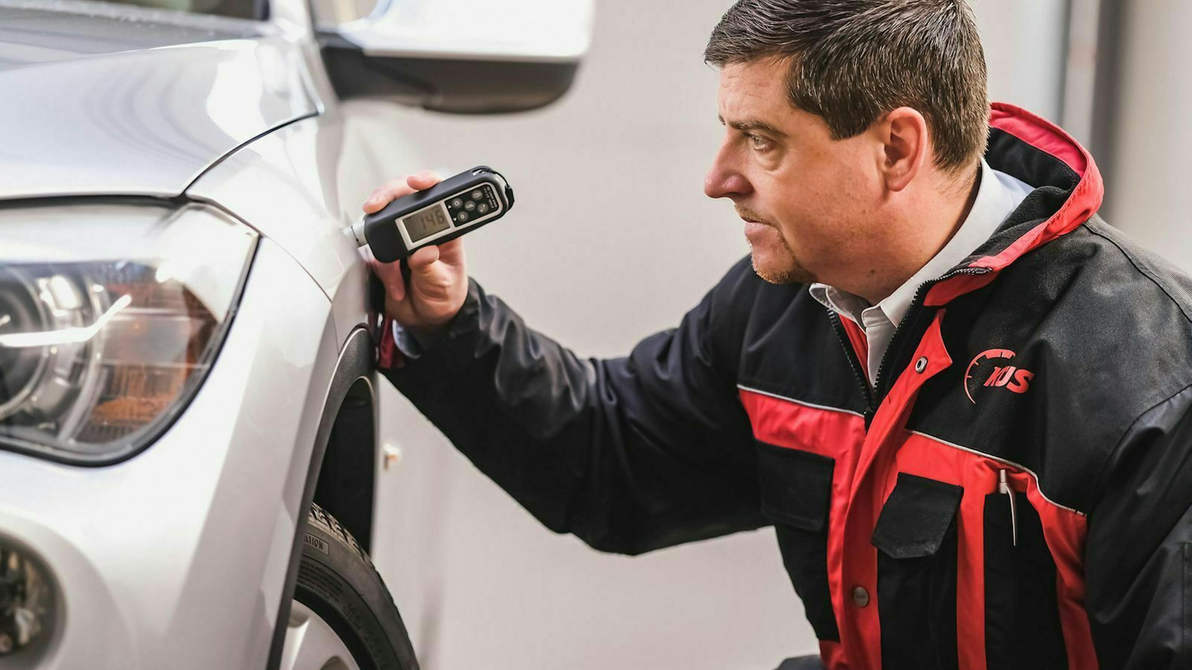 Prüfer mit einem Lackdicken-Messgerät misst die Schichtdicke am Kotflügel eines Autos.