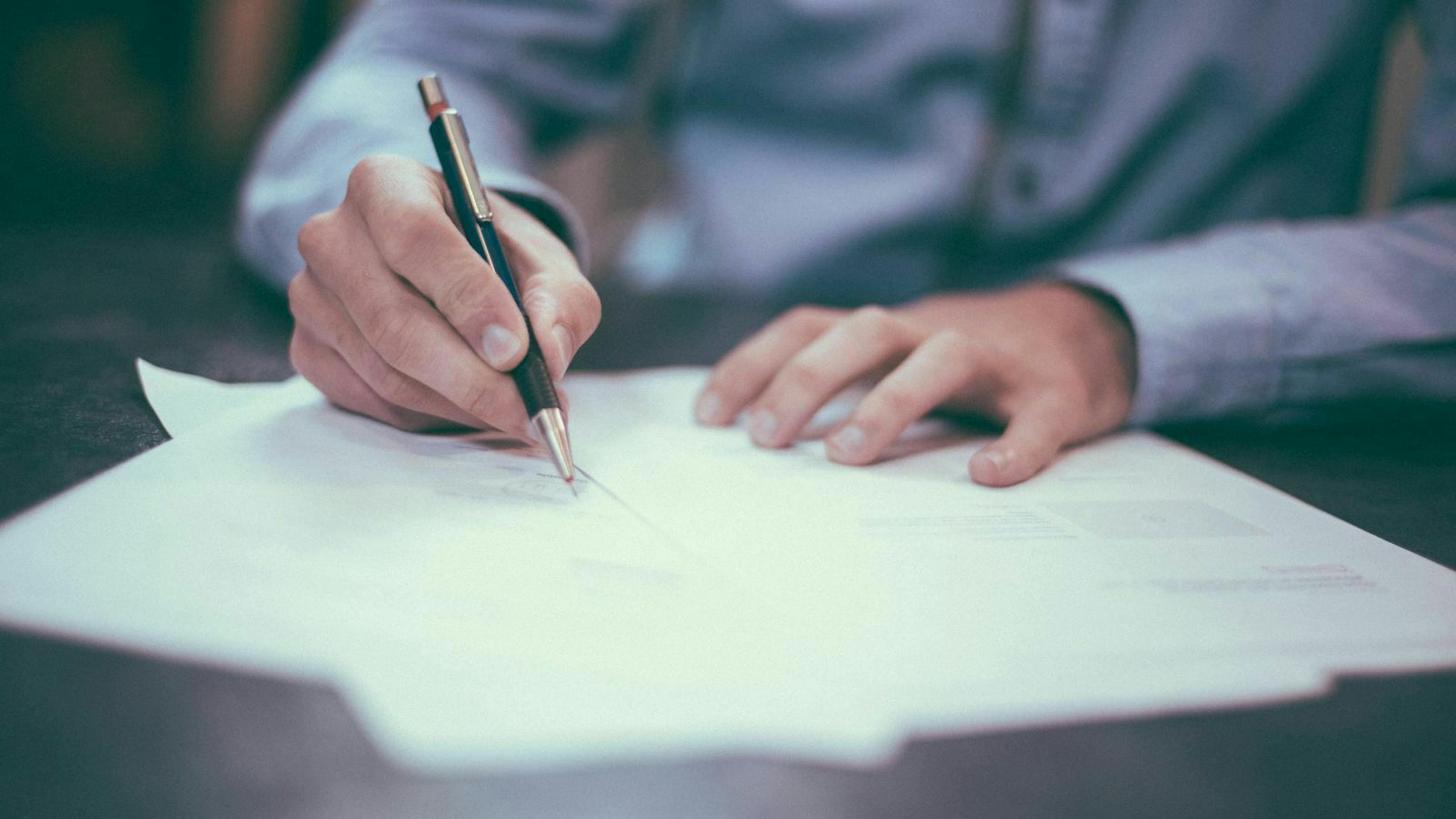 Ein Mann in einem hellblauen Hemd sitzt an einem Tisch und unterzeichnet einen Vertrag