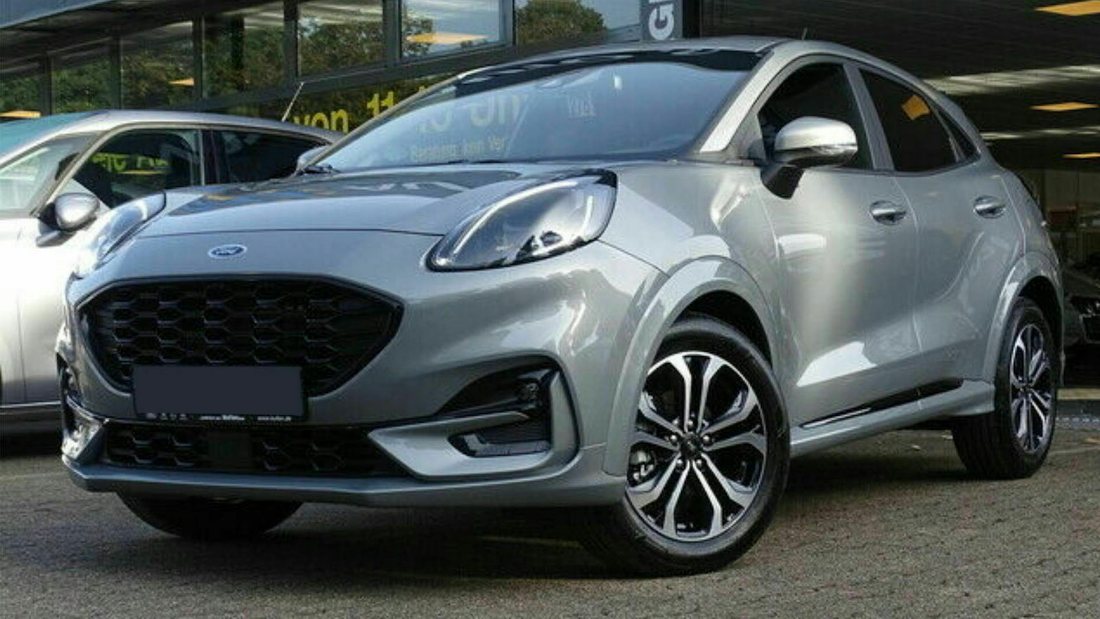 Ein silberner Ford Puma steht auf einem Parkplatz vor einem Gebäude mit Fensterfront