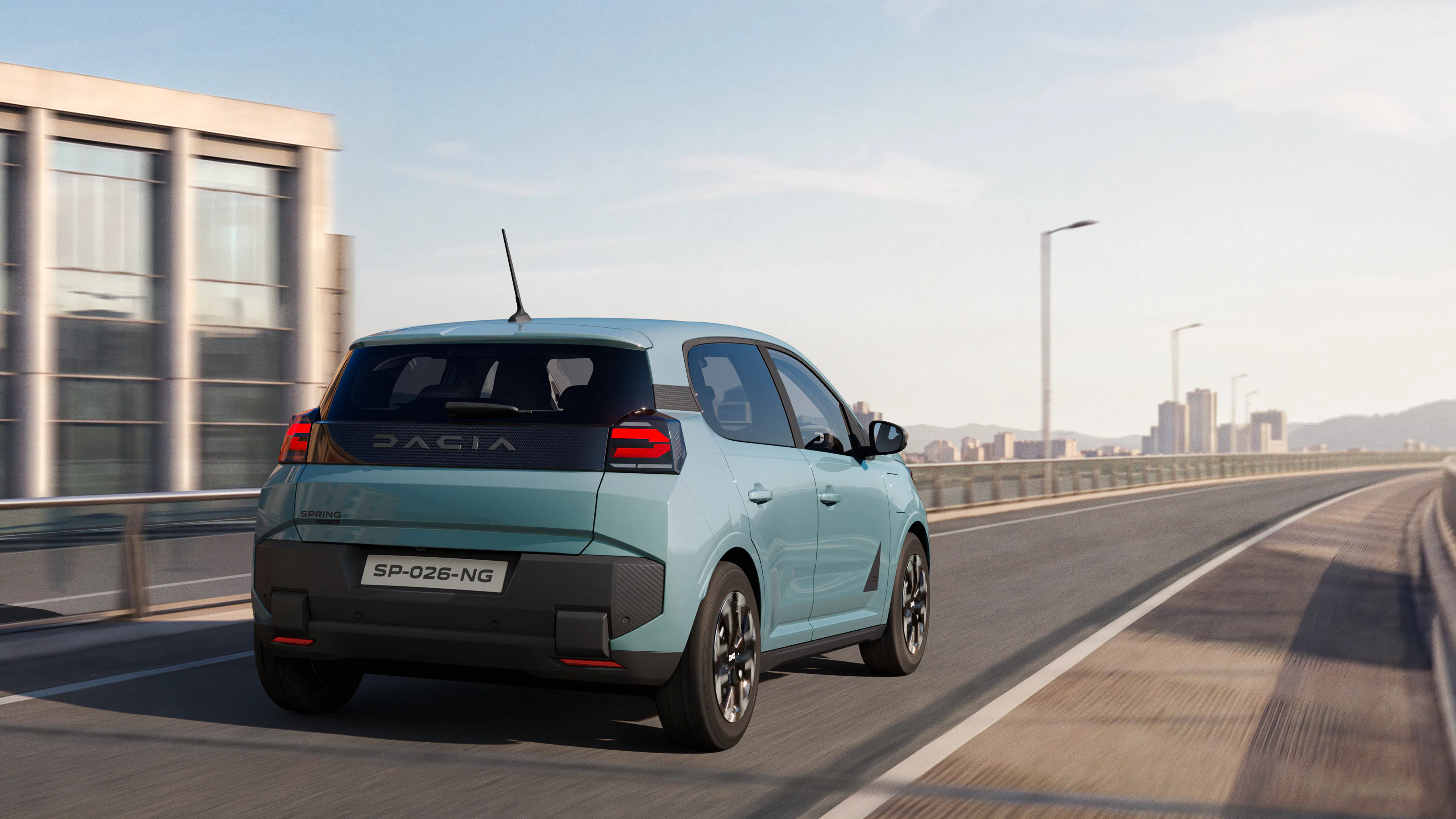 Heckansicht des fahrenden Dacia Spring 2 auf einer Straße vor einer Skyline.