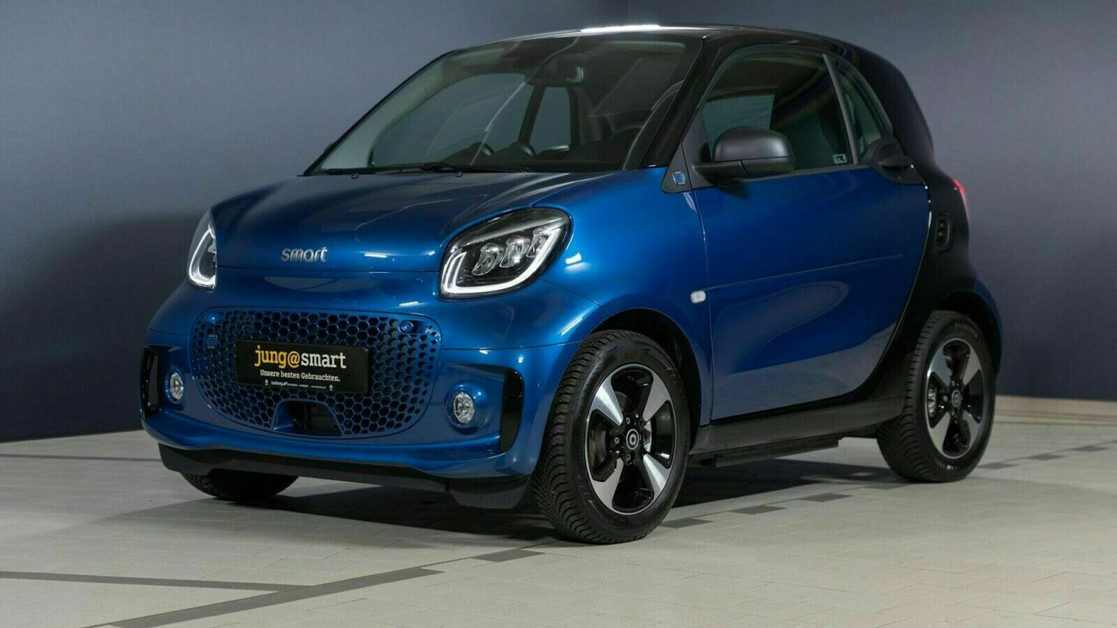 Ein blauer Smart Fortwo steht in einem Raum vor einer blauen Wand.