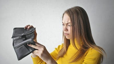 Eine junge Frau mit einem gelben Rollkragenpullover durchsucht einen schwarzen Geldbeutel