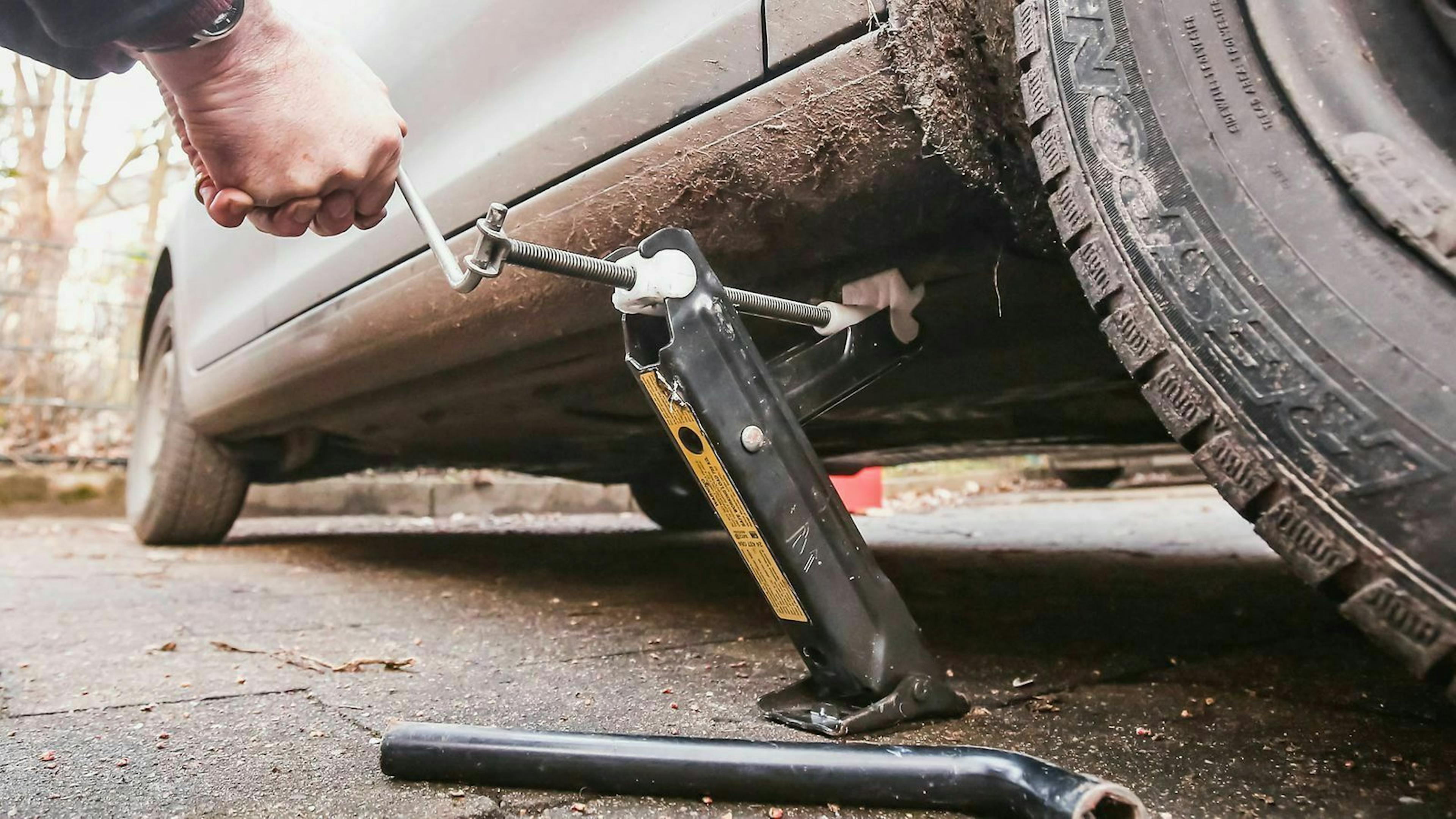 Jemand hat einen manuellen Wagenheber am Schweller montiert und kurbelt das Auto nach oben.