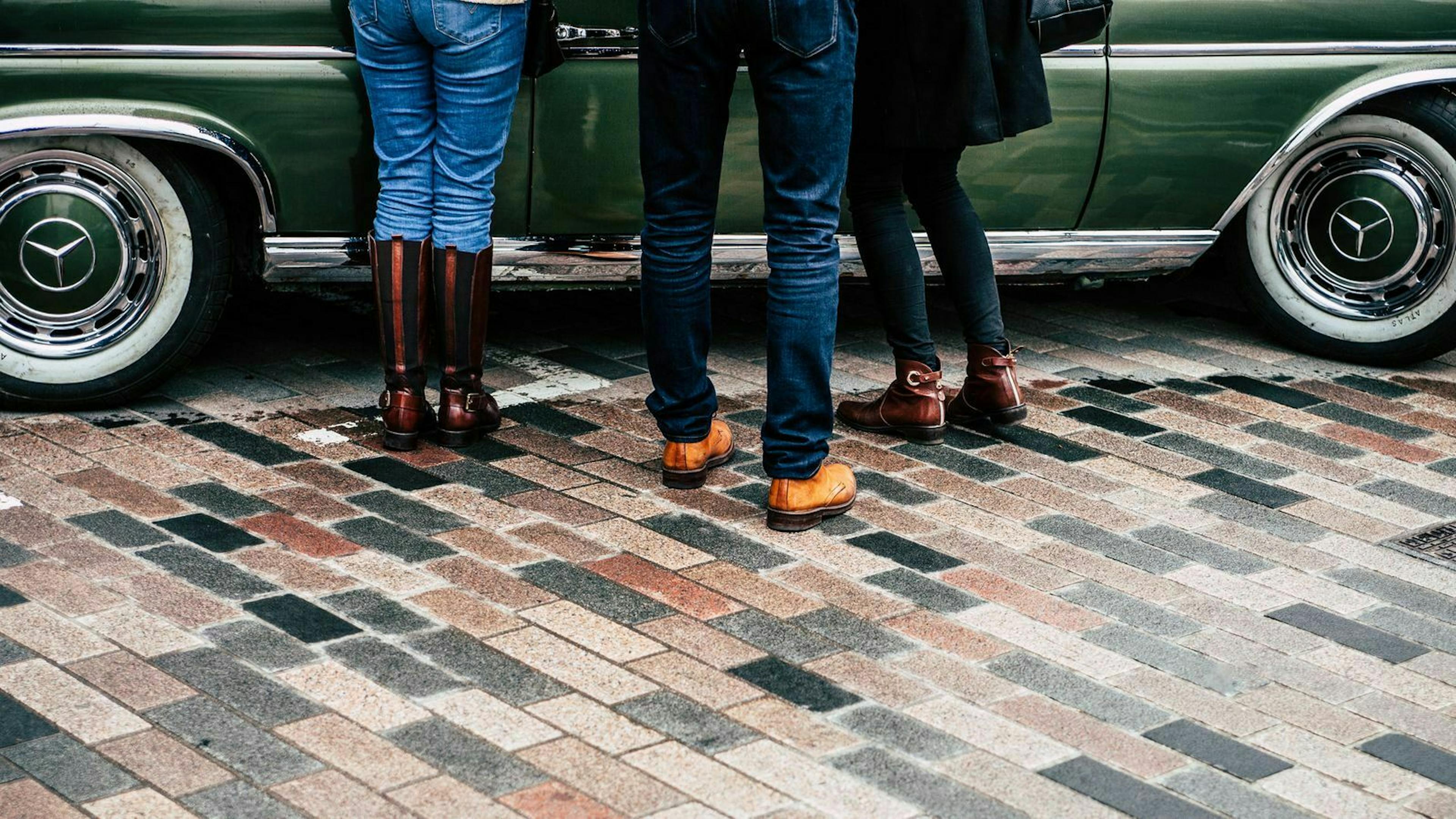 Drei Menschen nehmen ein Auto vor dem Gebrauchtwagenkauf genau unter die Lupe. 