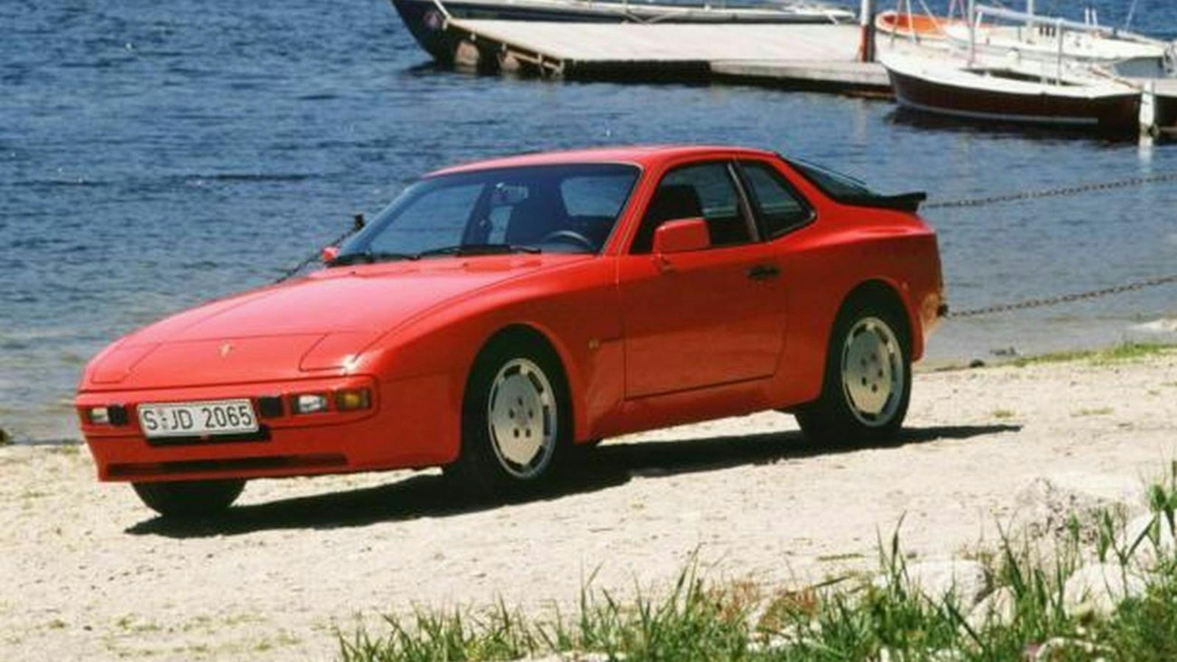 Ein roter Porsche 944 Oldtimer steht am Ufer eines Sees.