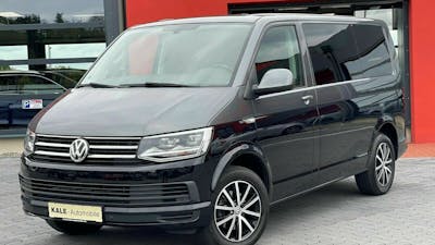 Ein schwarzer VW Multivan steht vor einem Gebäude mit rot-grauer Fassade