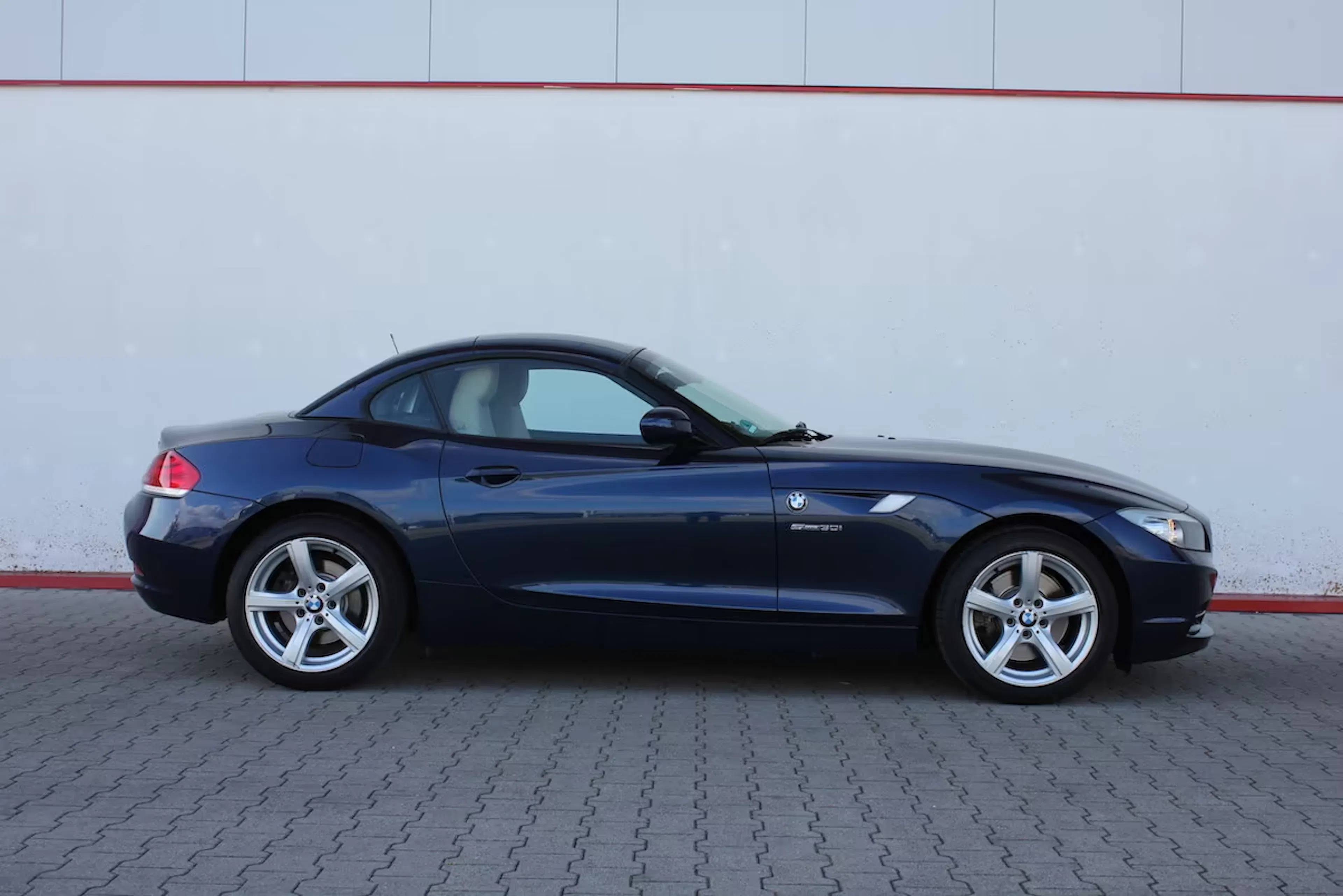Dunkelblauer BMW Z4 mit geschlossenem Verdeck vor einer weißen Wand.