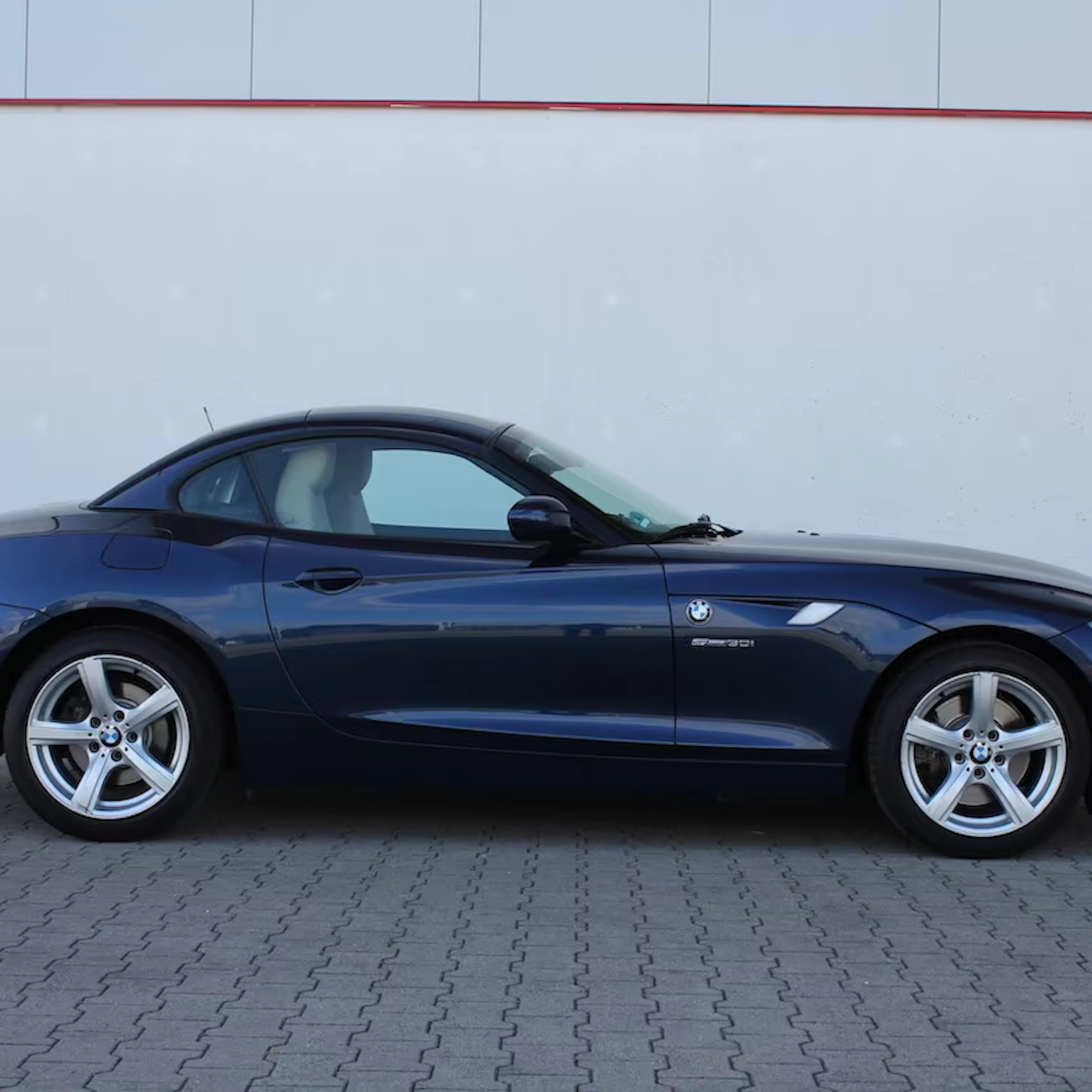Dunkelblauer BMW Z4 mit geschlossenem Verdeck vor einer weißen Wand.