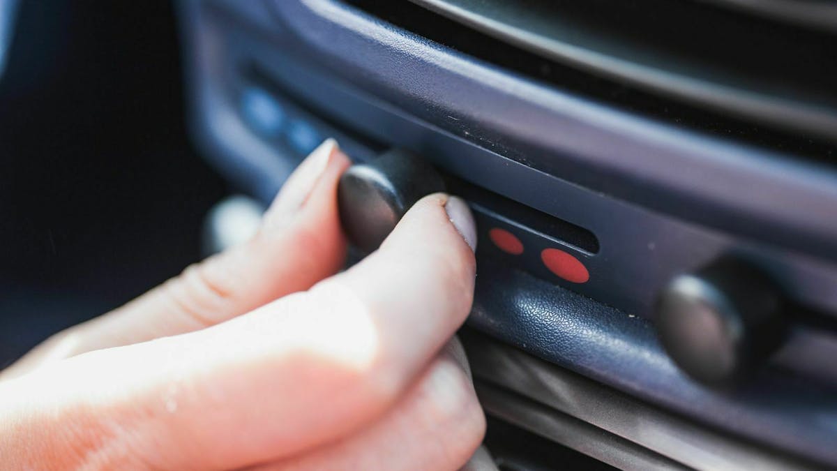 Eine Hand greift zum Lüftungs-Regler im Auto.