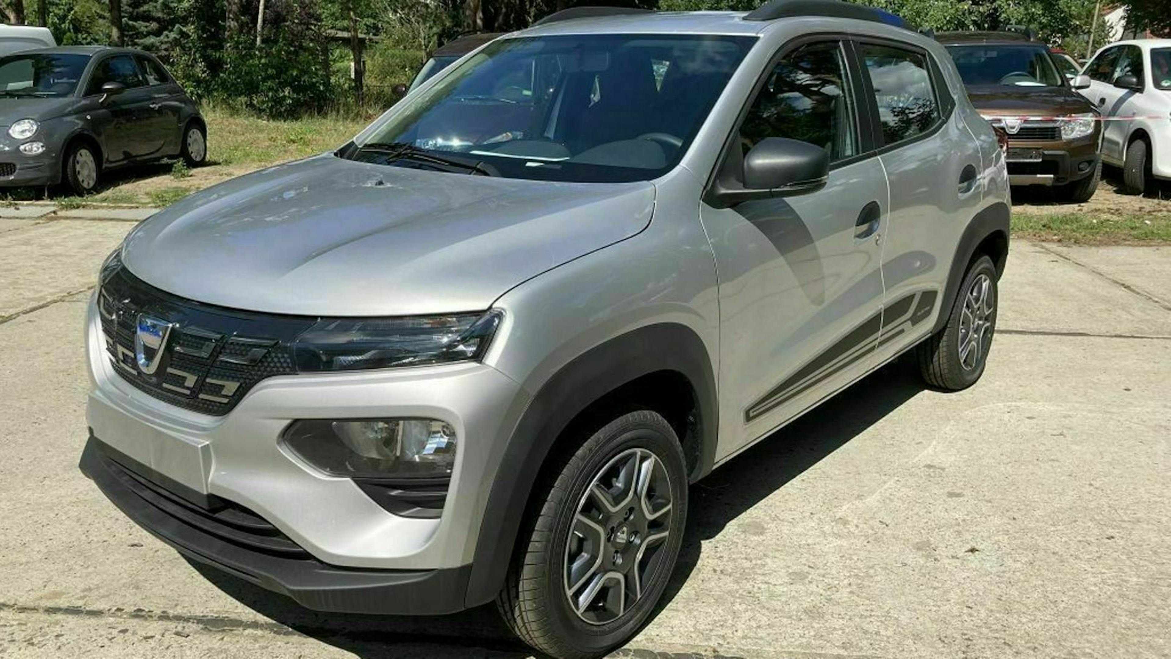 Ein silberner Dacia Spring steht auf einem Parkplatz.