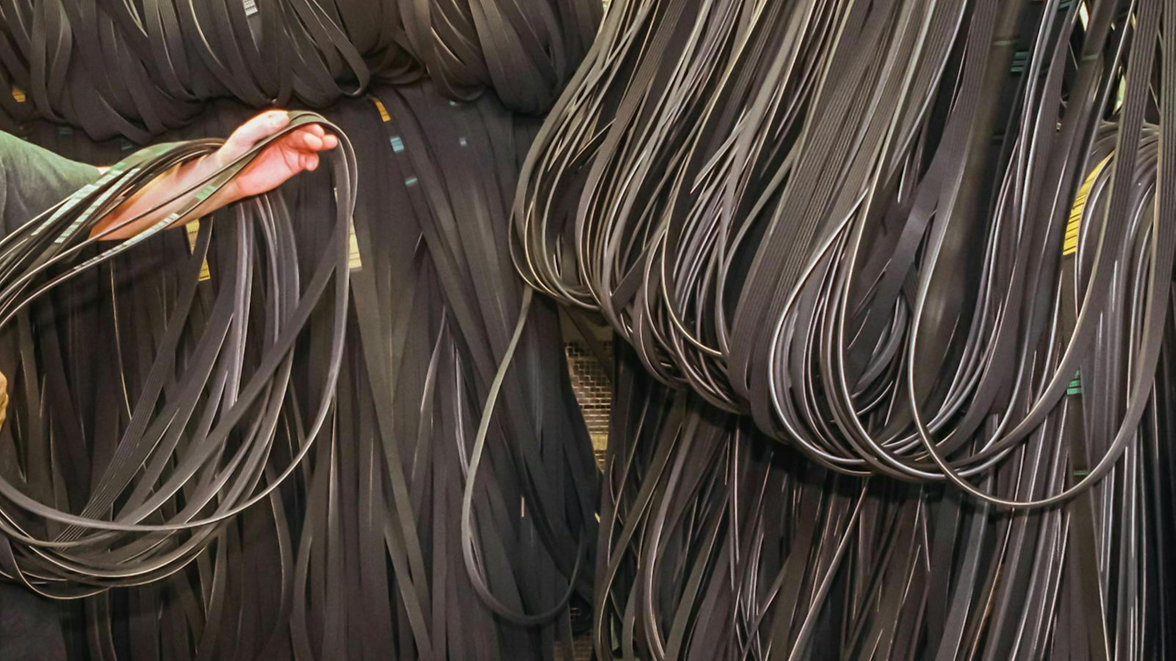 Jemand hält einen Keilriemen in der Hand während er durch ein Lager von Keilriemen geht.