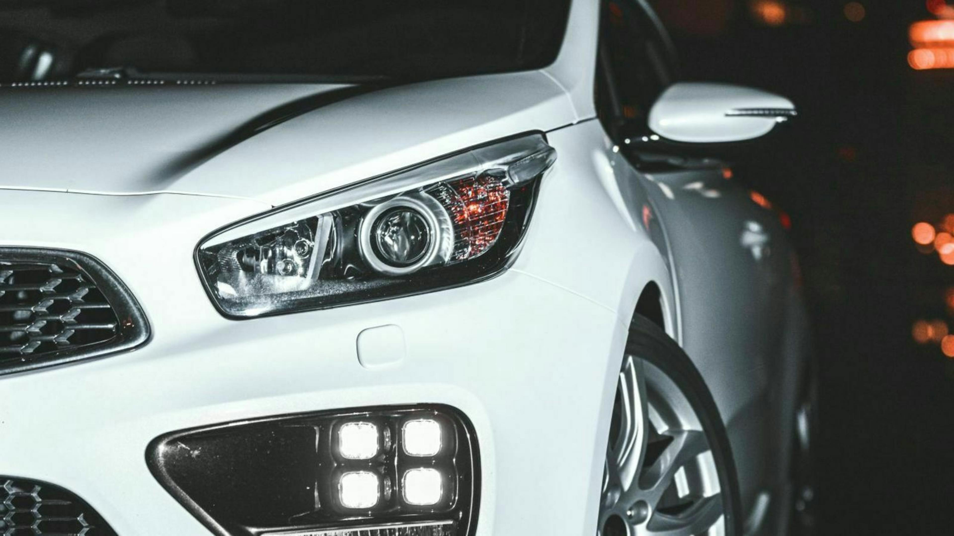 Nahaufnahme eines weißen Autos mit modernen Scheinwerfern und Chromdetails, vor einem dunklen Hintergrund.