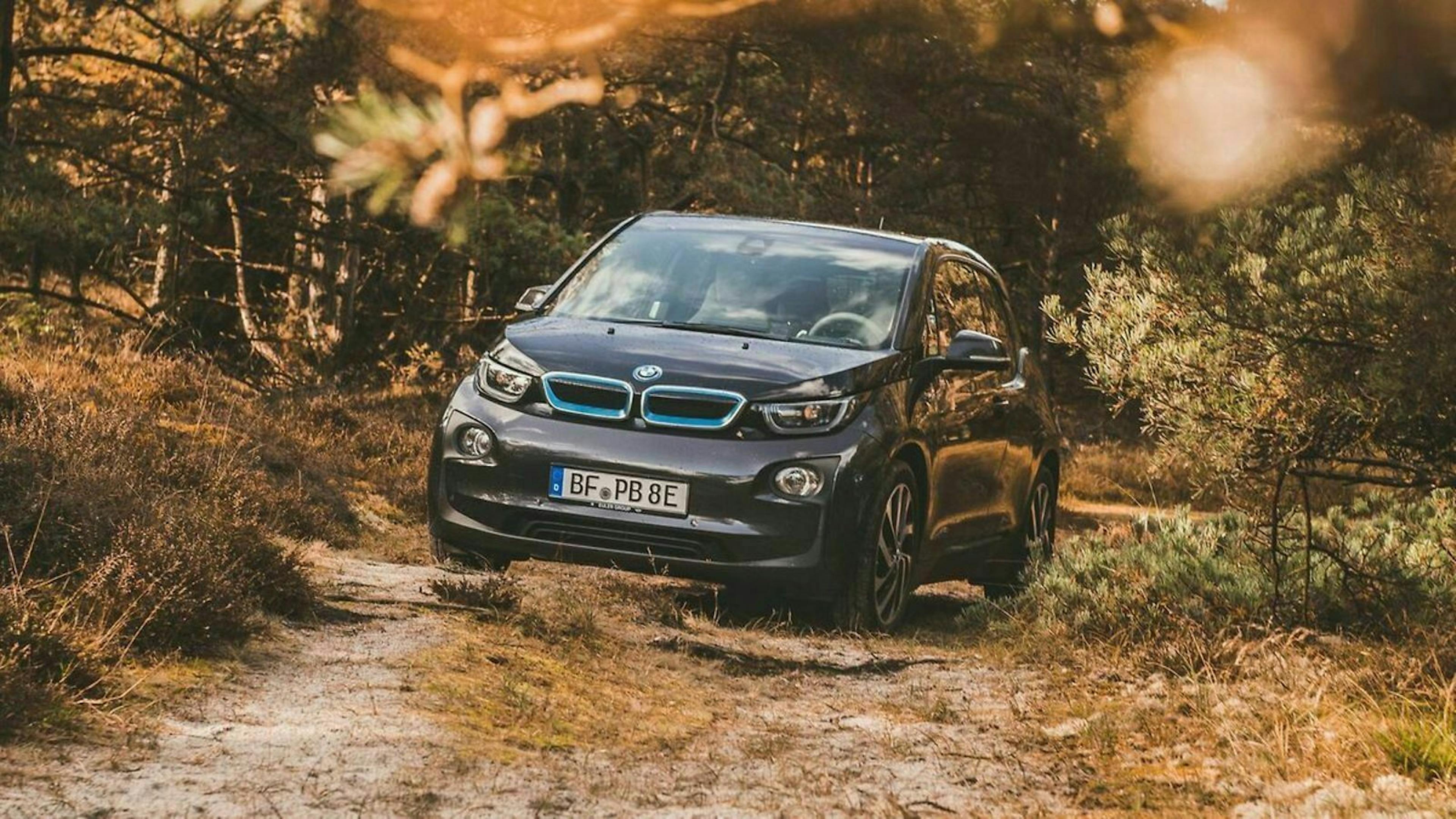 Ein BMWi3 steht auf einem Waldweg.