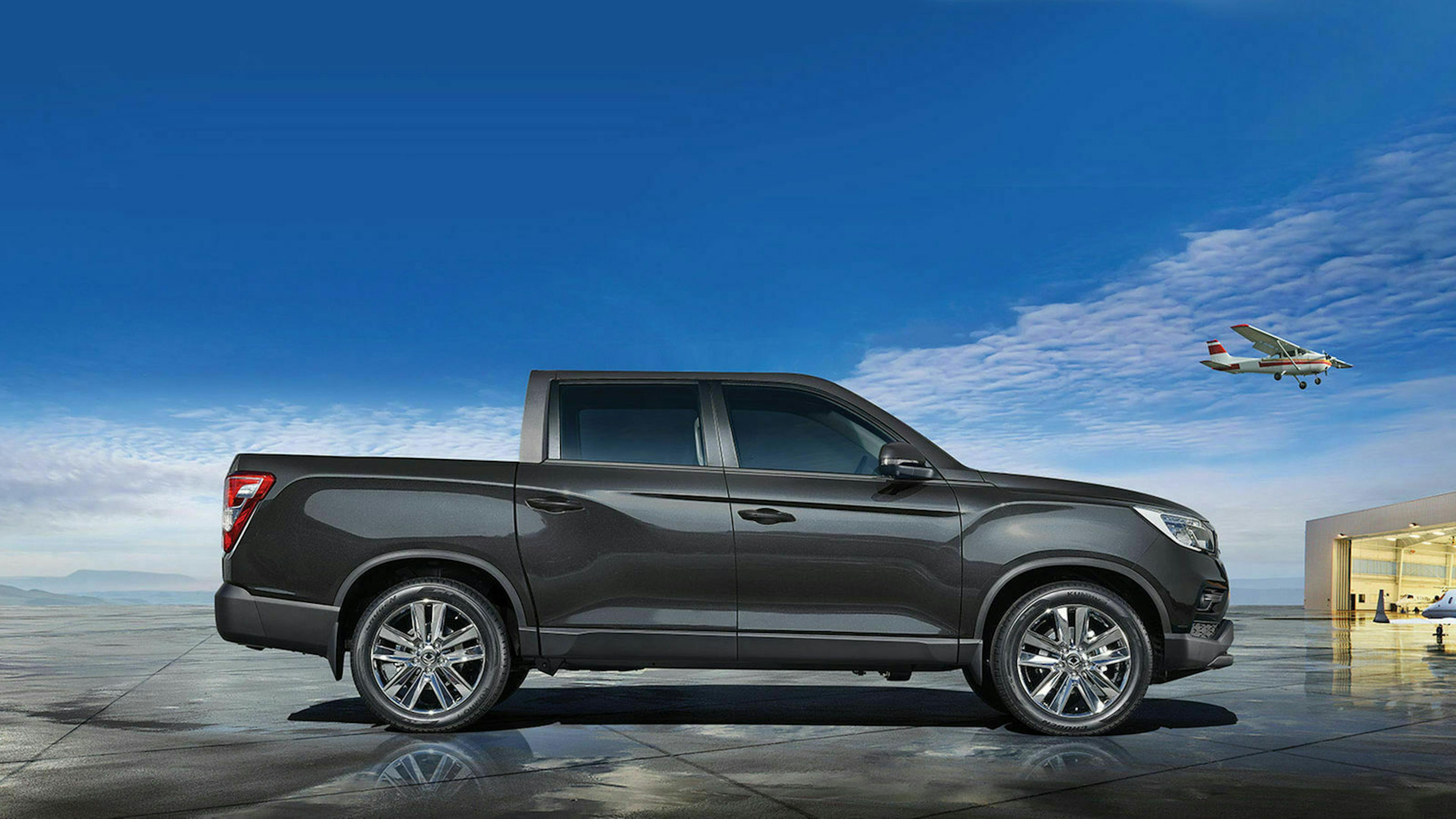 Seitenansicht eines grauen Ssangyong Musso, der auf einem Flugplatz steht.