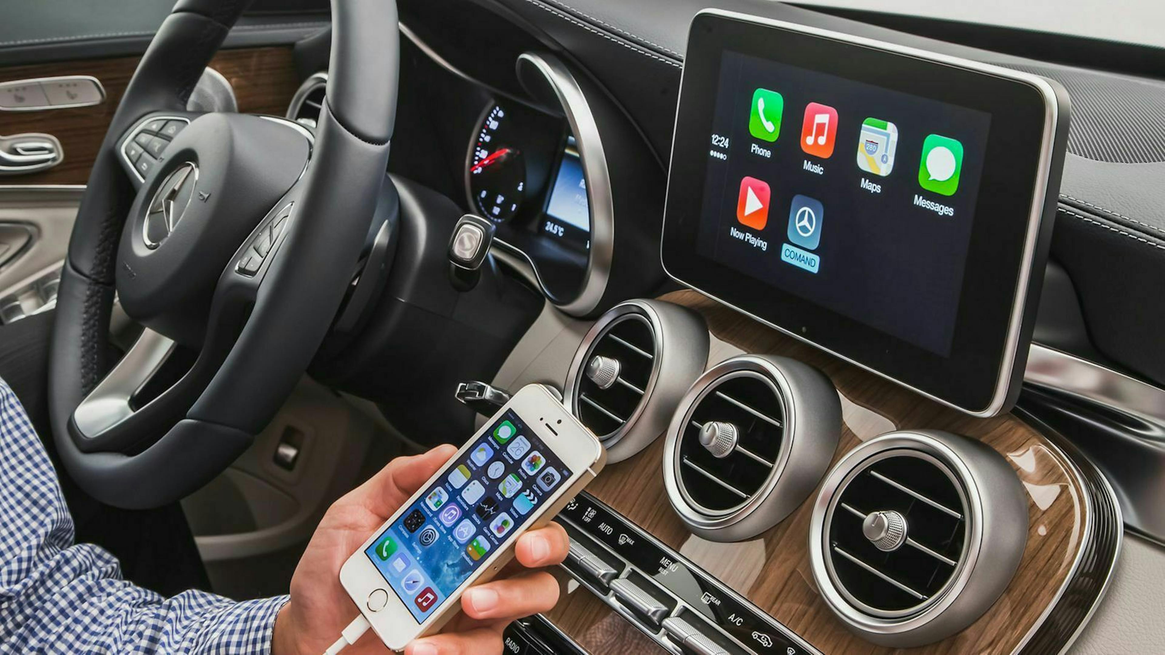 Jemand sitzt im Auto und hält ein Smartphone in der Hand, auf dem Bildschirm des Autos werden die Inhalte des Handys wiedergegen