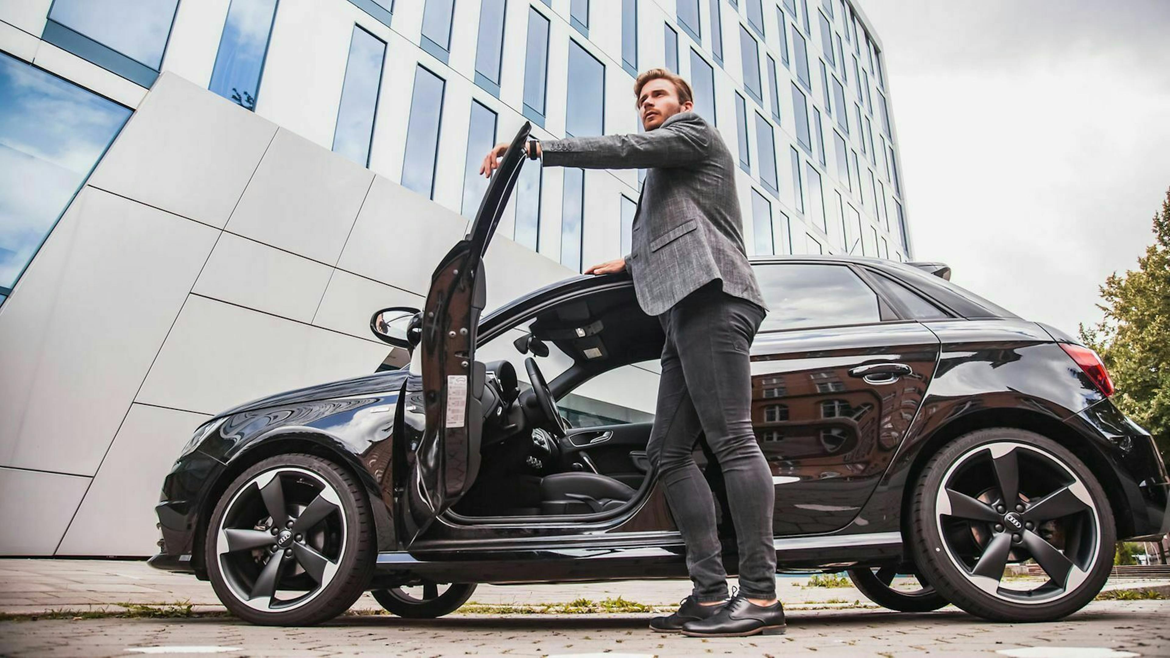 Ein Mann im Anzug ist im Begriff, in seinen Dienstwagen einzusteigen.