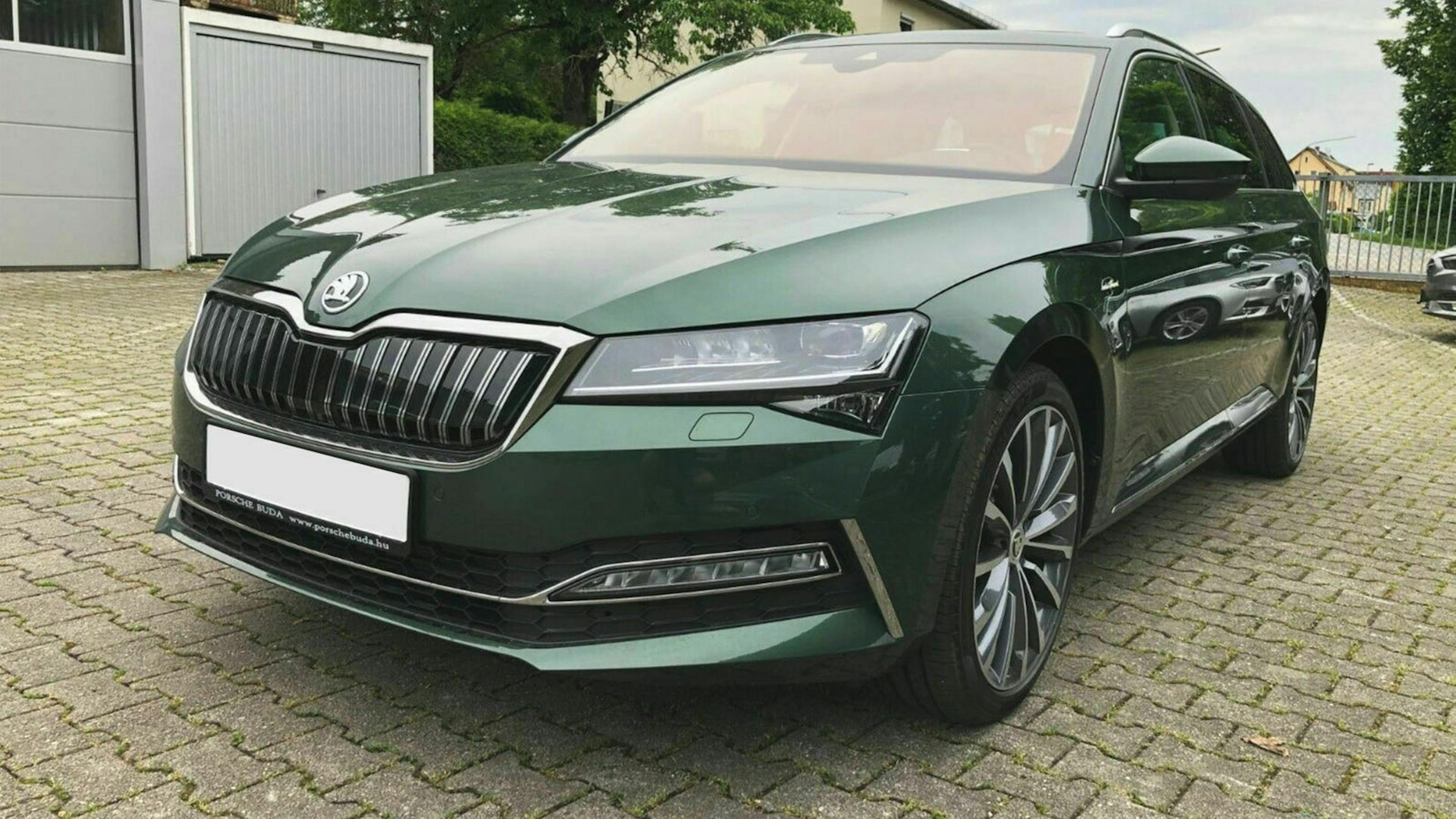Ein dunkelgrüner Skoda Superb steht vor einer weißen Garage