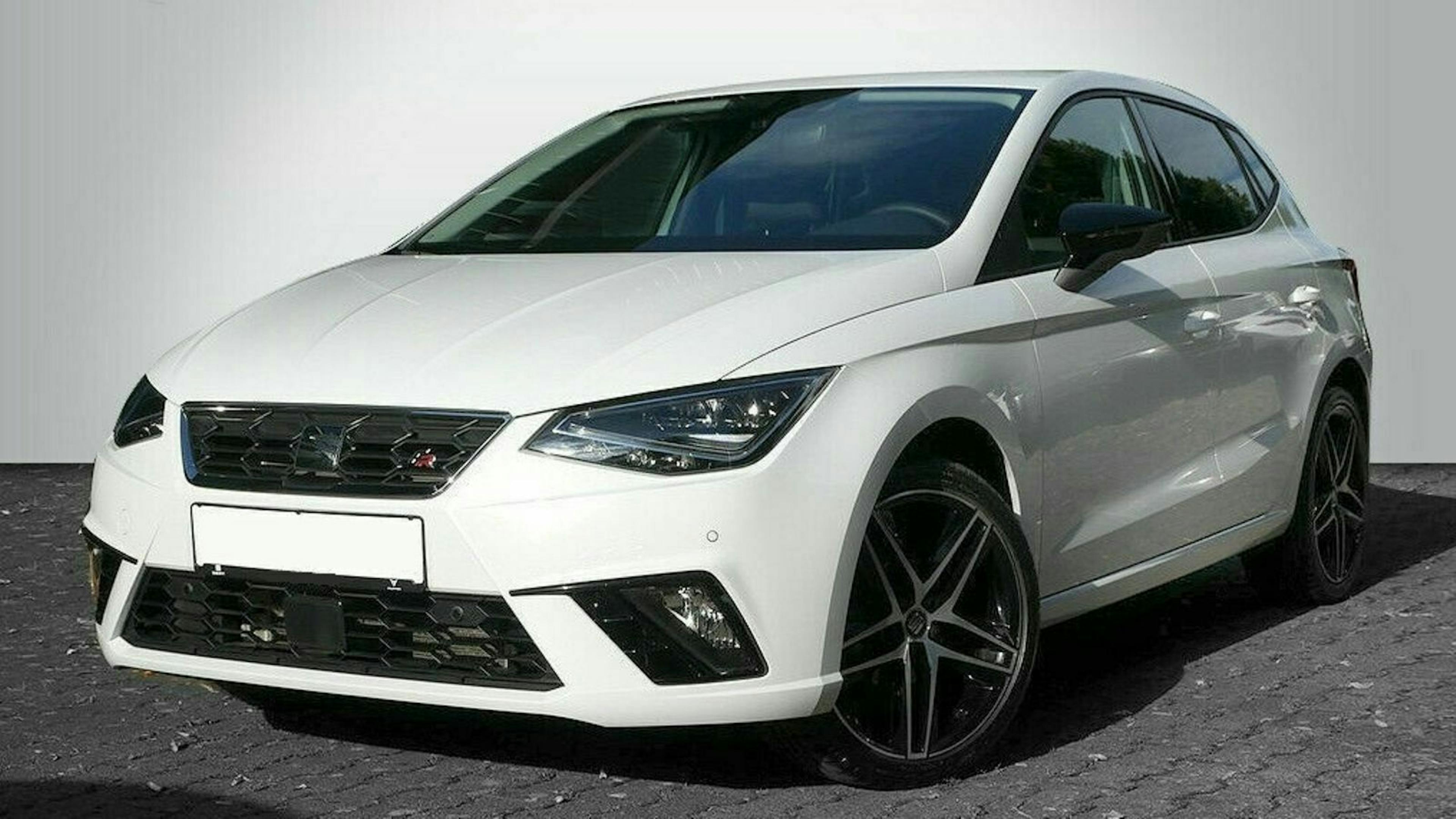 Weißer Kompaktwagen mit sportlichem Design und schwarzen Felgen, fotografiert auf Pflastersteinen vor einem grauen Hintergrund.