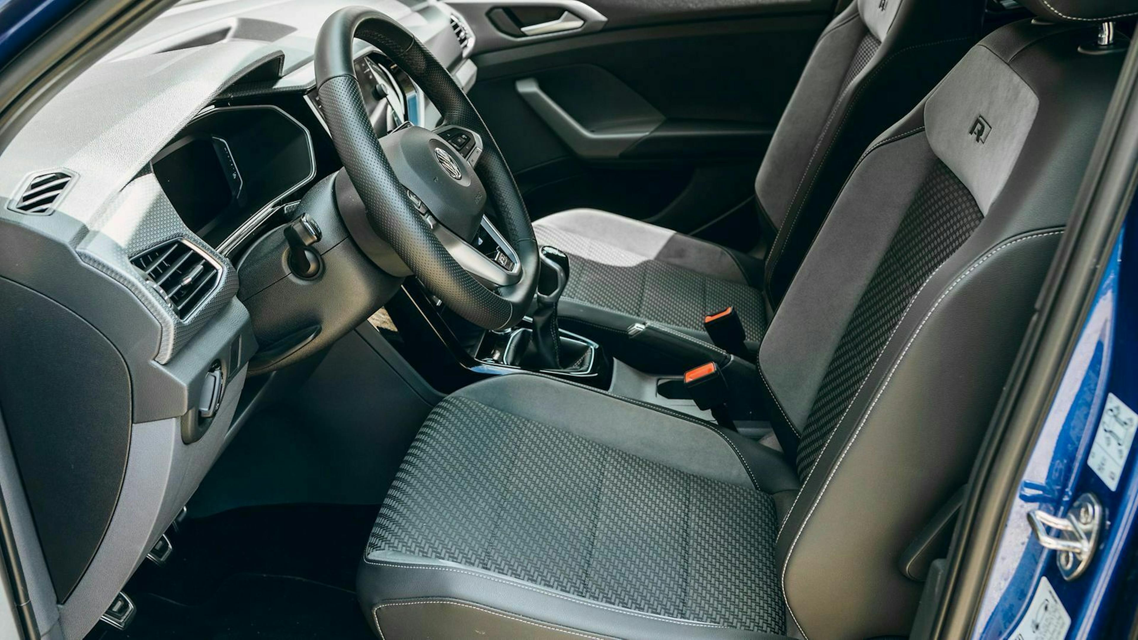 Innenraum eines Autos mit grauen Sitzen, modernem Lenkrad und Mittelkonsole. Die Türverkleidung ist in Blau gehalten.