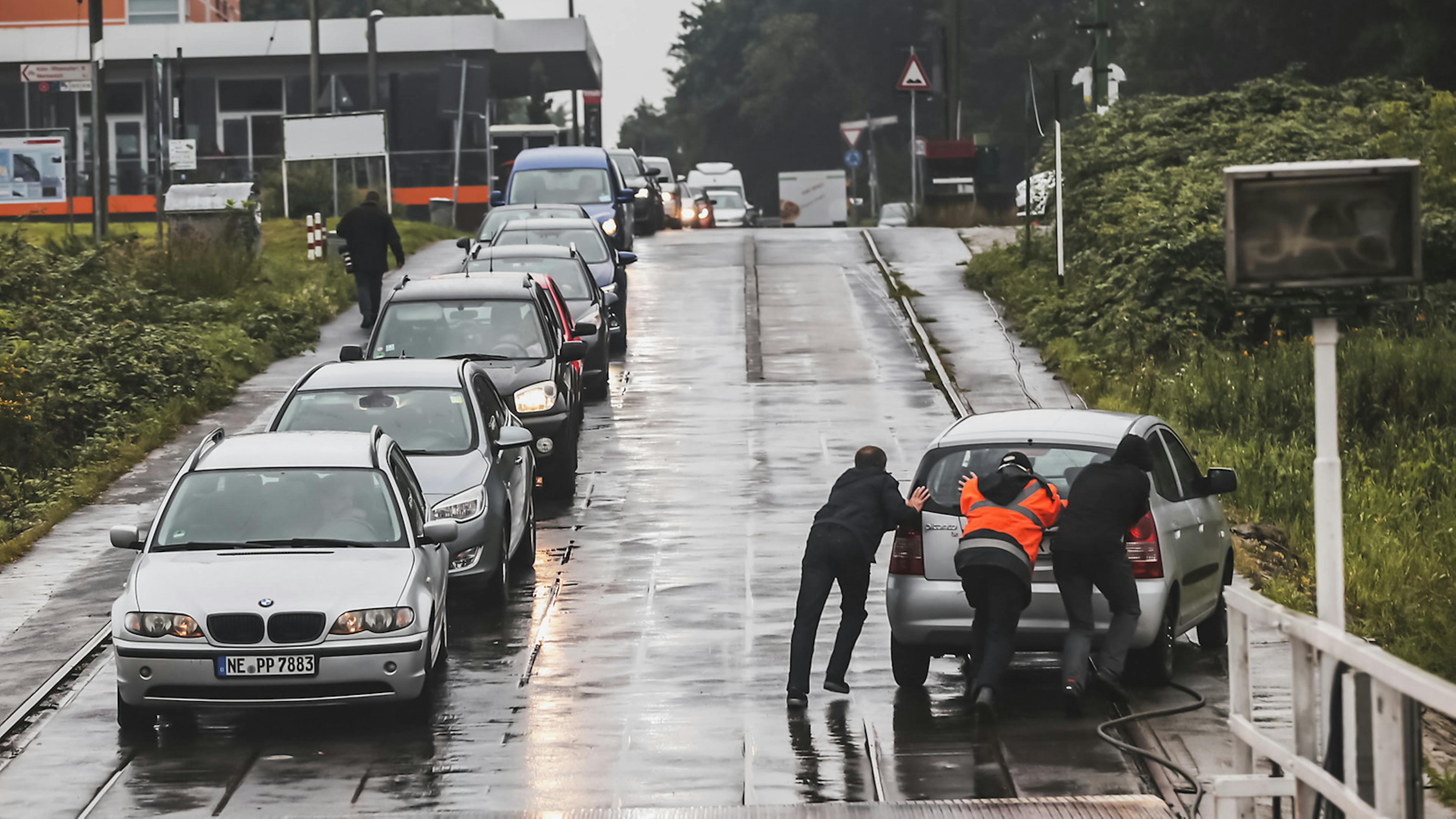Eine Gruppe Menschen schiebt ein liegen gebliebenes Auto im Regen an den Straßenrand