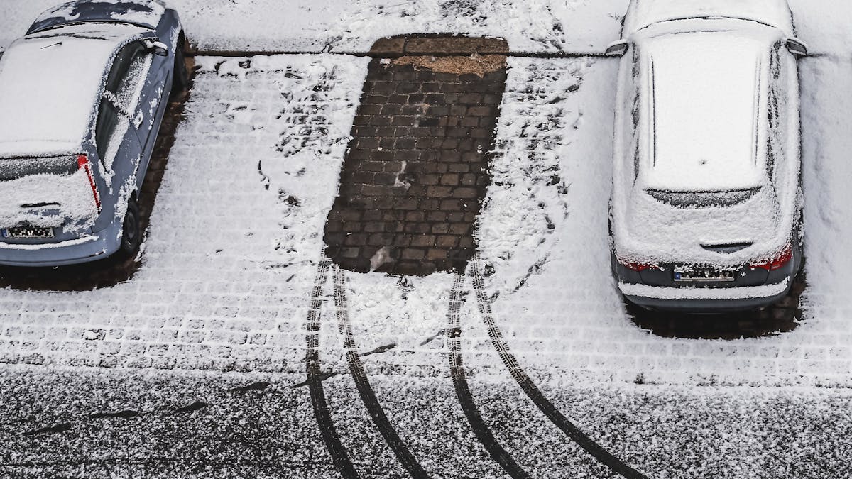 Auf einem Parkplatz hat es frisch geschneit. Ein Auto stand in der Mitte und hinterließ Spuren im Schnee.