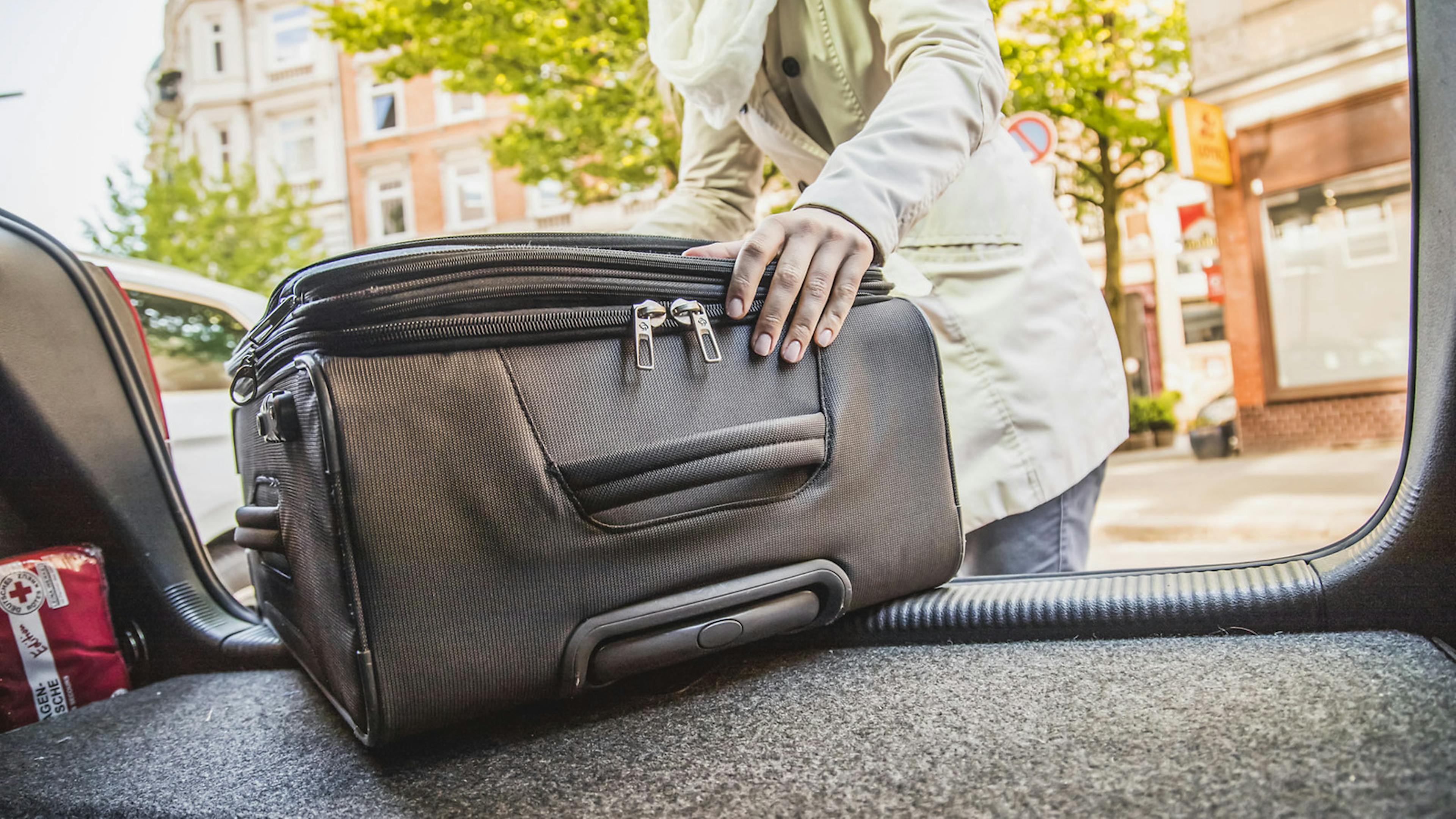 Frau lädt Koffer in den Kofferraum