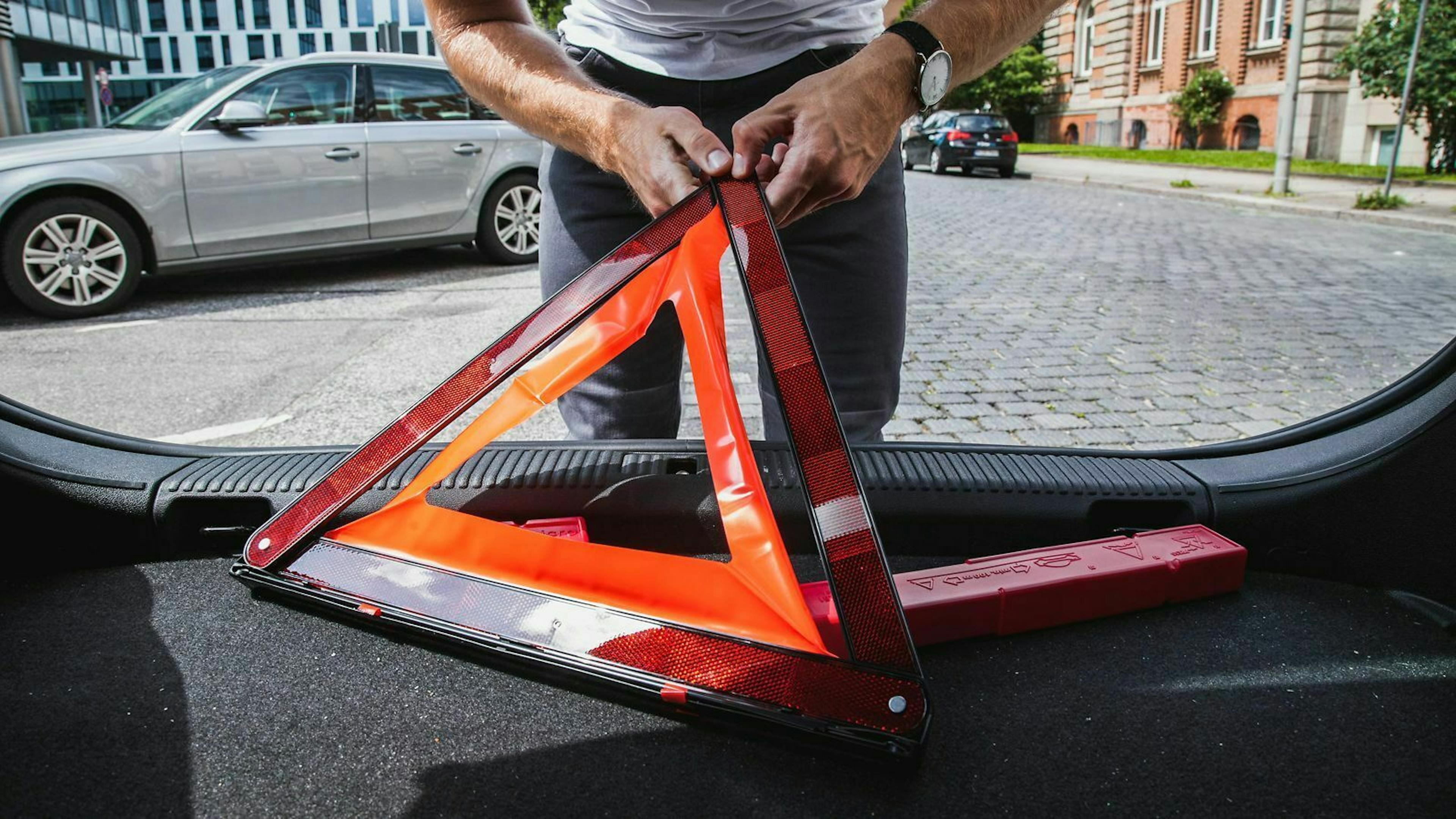 Ein Warndreieck besteht aus drei zusammengesetzten Balken, die rot reflektieren, und einem standsicheren Fuß.