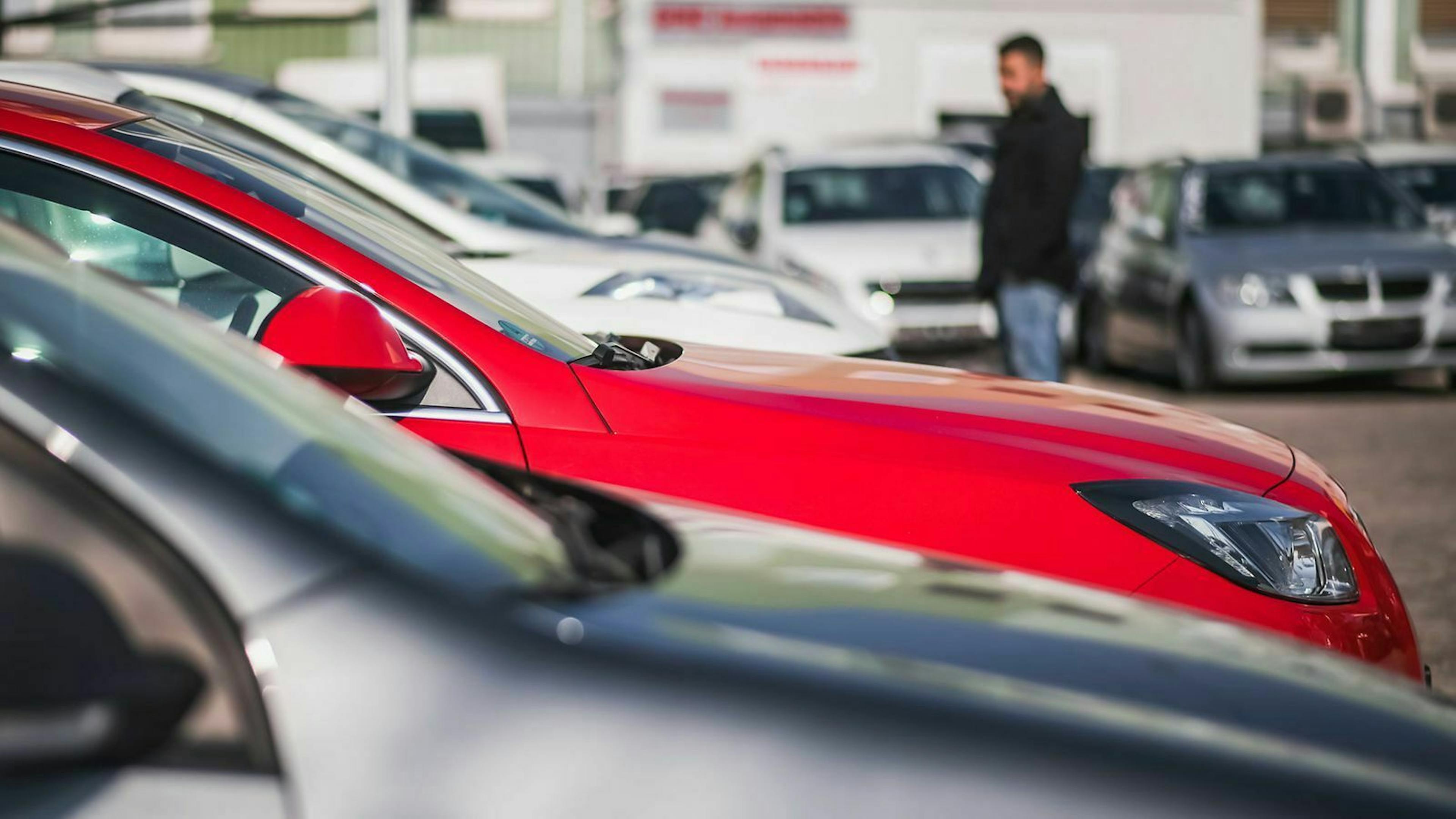 Autos stehen auf einer mobile.de-Ankaufsstation in Reihe geparkt während sich im Hintergrund ein Mann Autos ansieht.