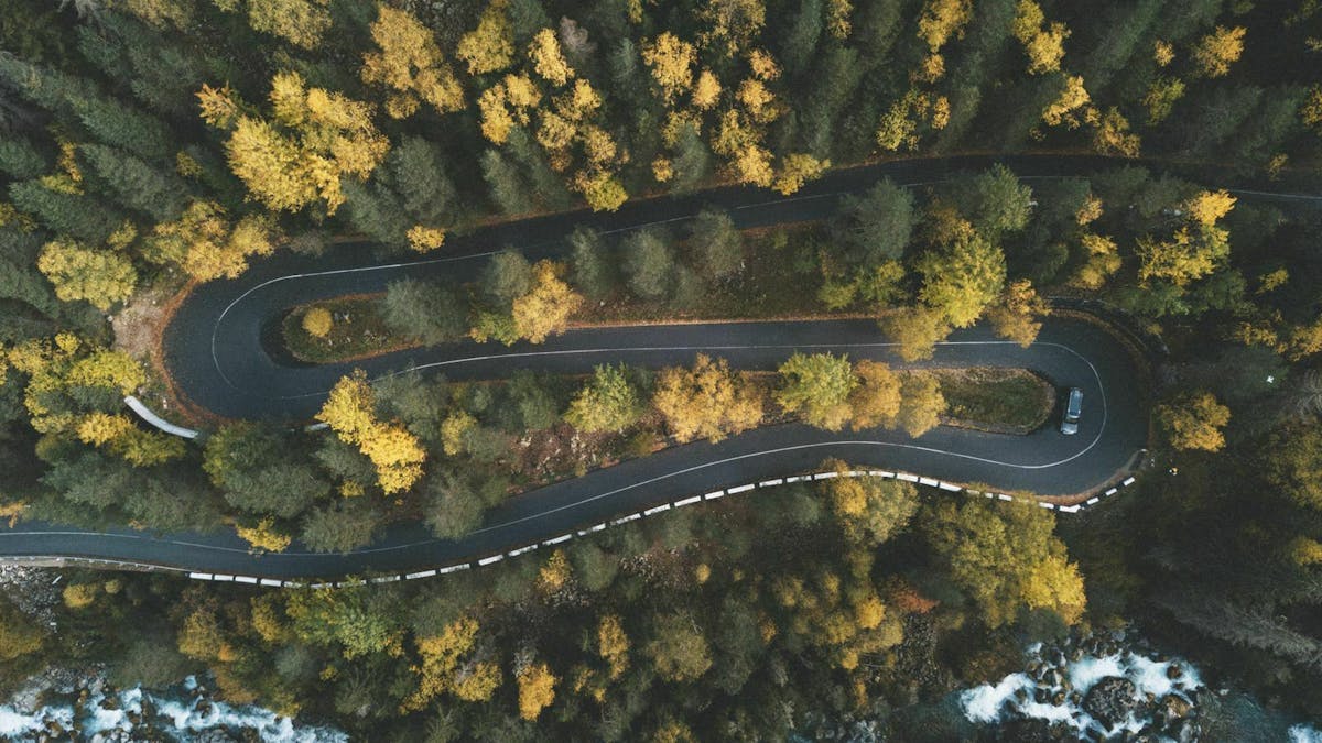 Ein blauer PKW fährt eine kurvige Bergstraße entlang, die durch einen Wald verläuft