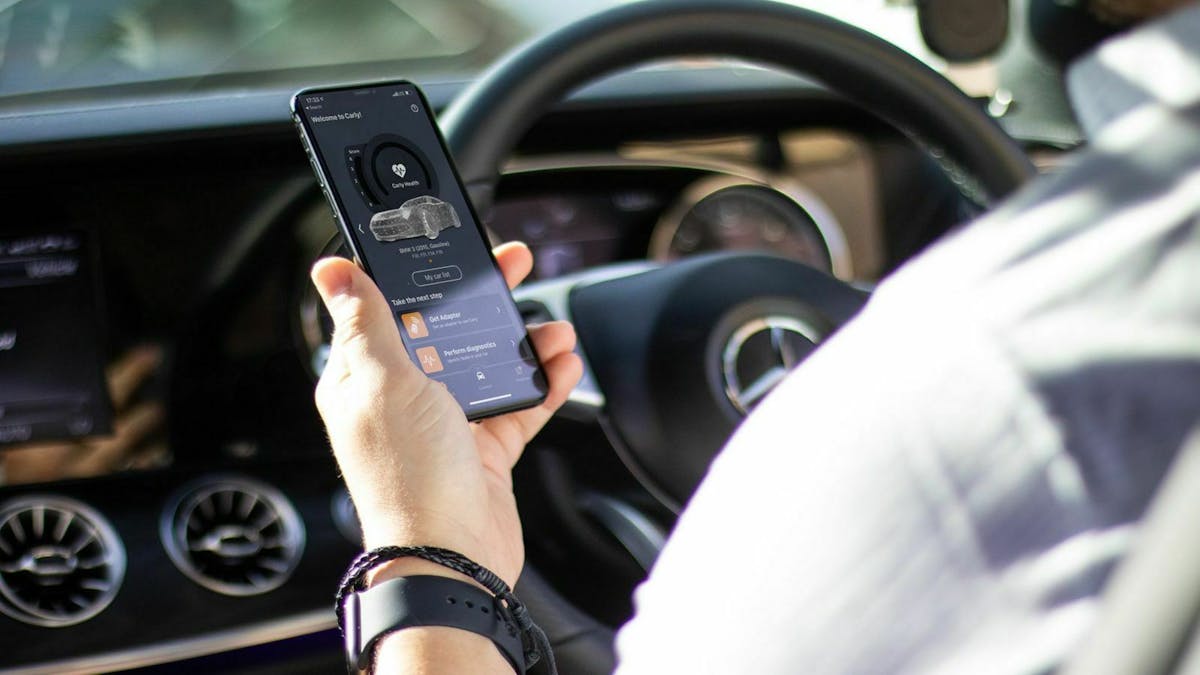 Zu sehen ist ein Smartphone in der Hand eines Autofahrers beim Fahren