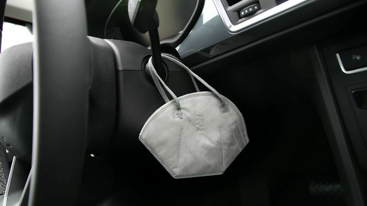 Eine FFP2-Maske hängt im Cockpit eines PKW