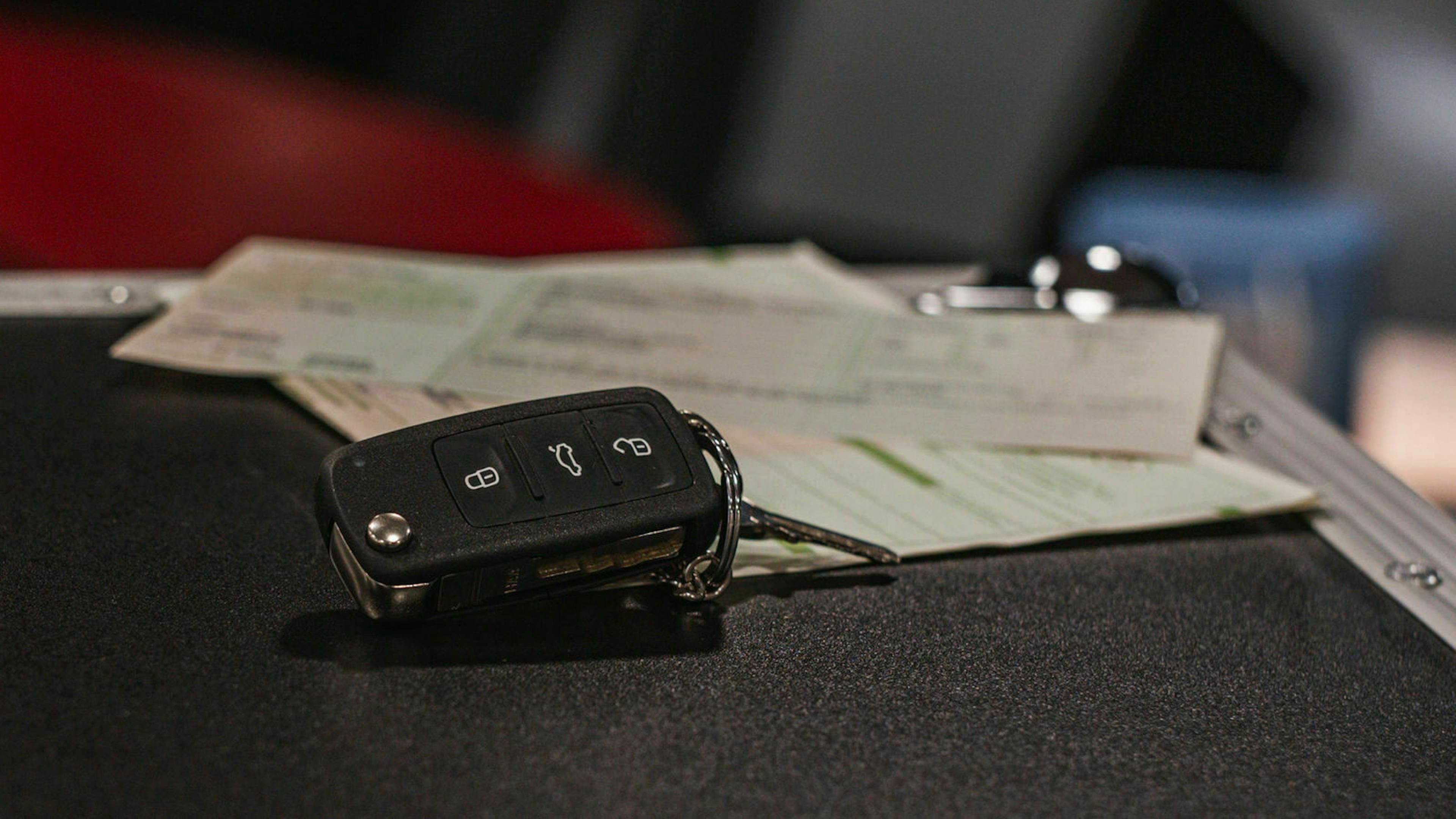 Ein Autosschlüssel liegt auf einem Tisch. Dahinter die Zulassungsbescheinigungen 1 und 2